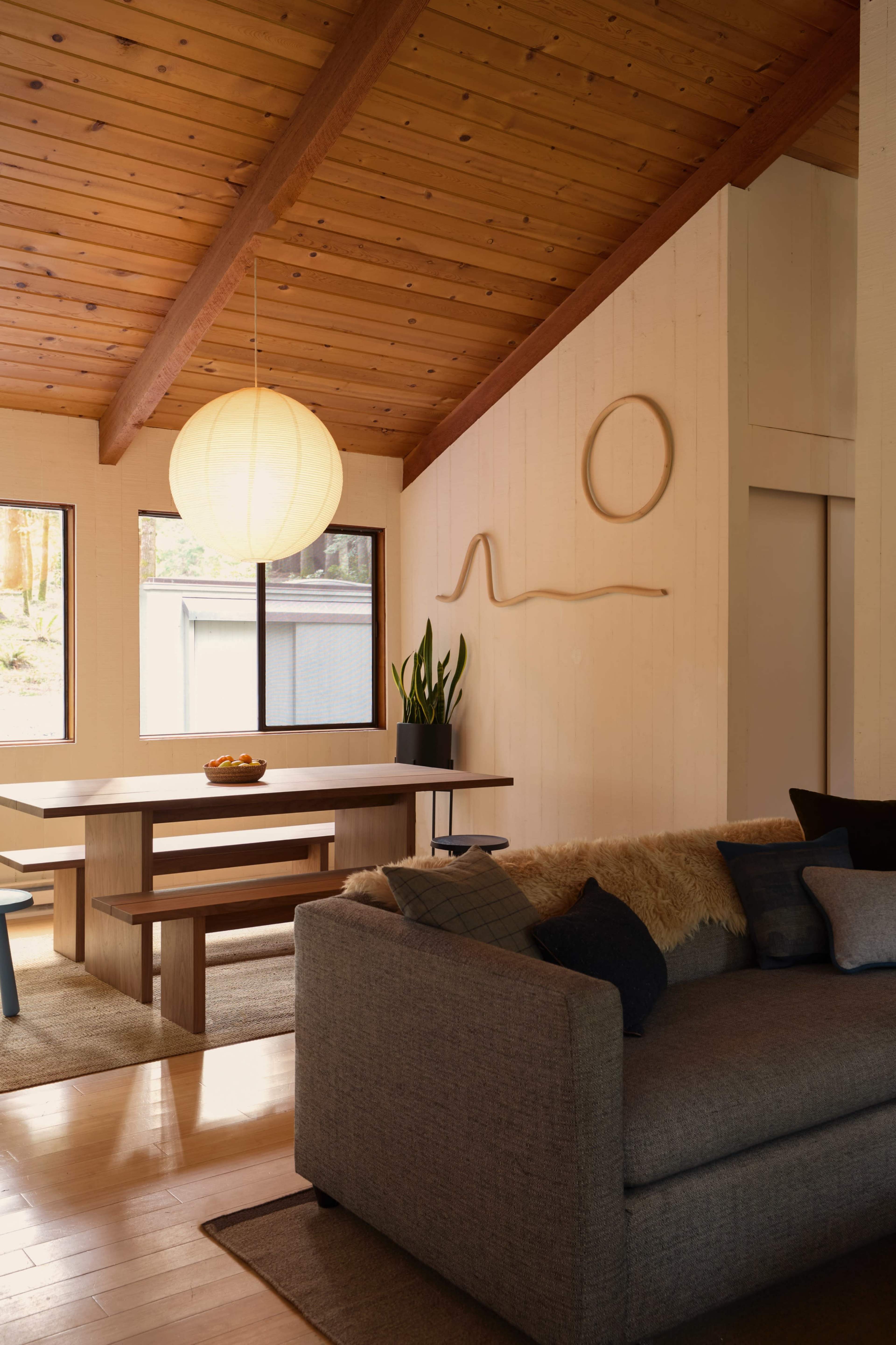 A living space features a wooden ceiling, a round paper lantern, a table with fruit, and a sofa with various cushions.