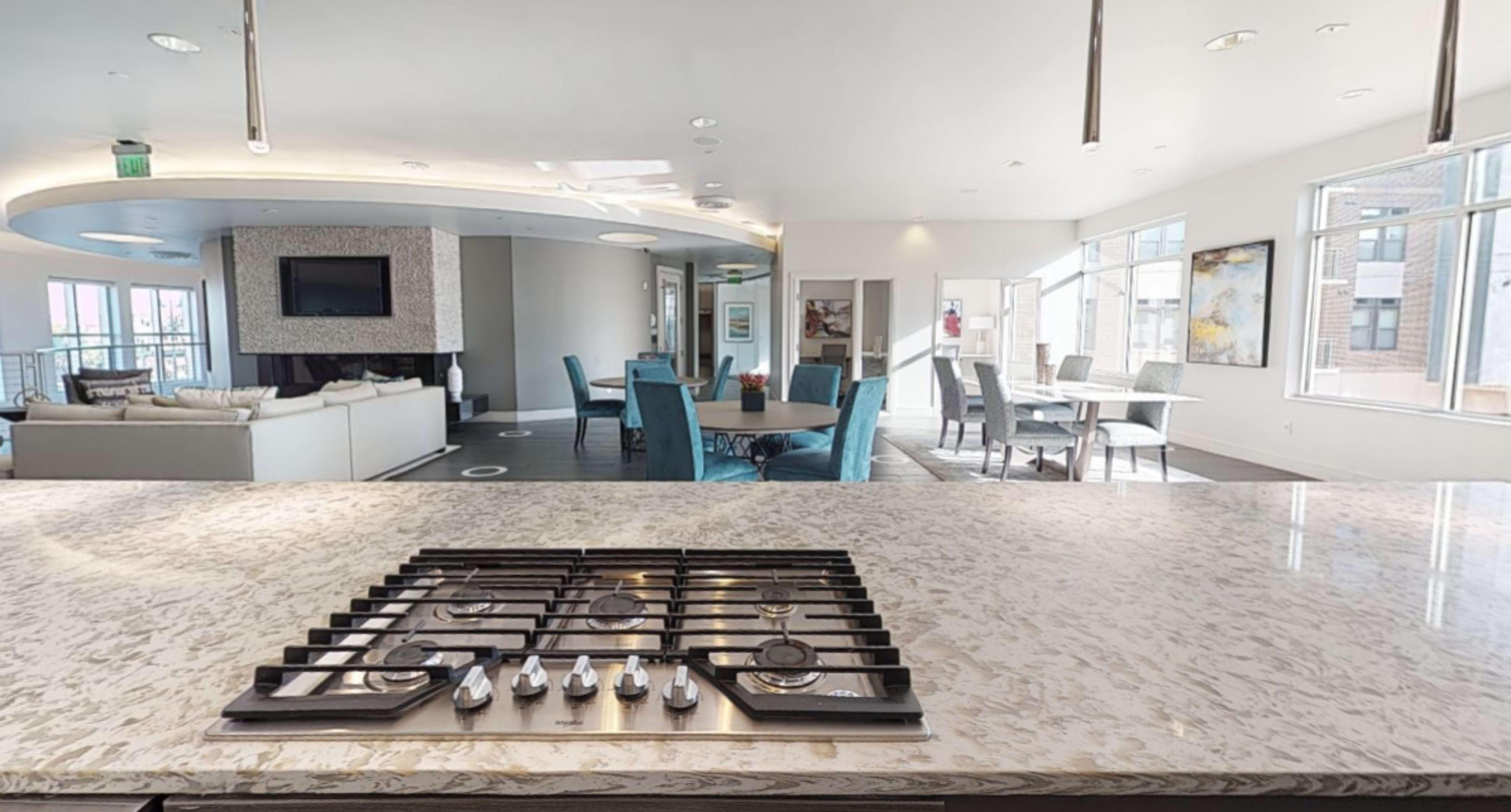 A modern open-concept kitchen with a gas stove in the foreground and a furnished living area visible in the background.