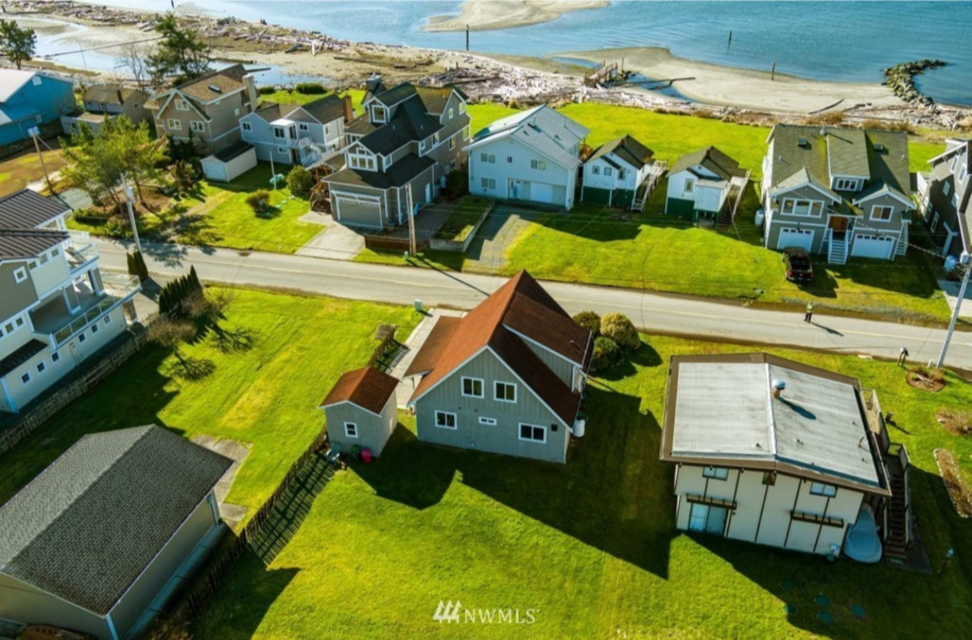 A coastal neighborhood with several houses, a road running through it, and a beach area visible in the background.