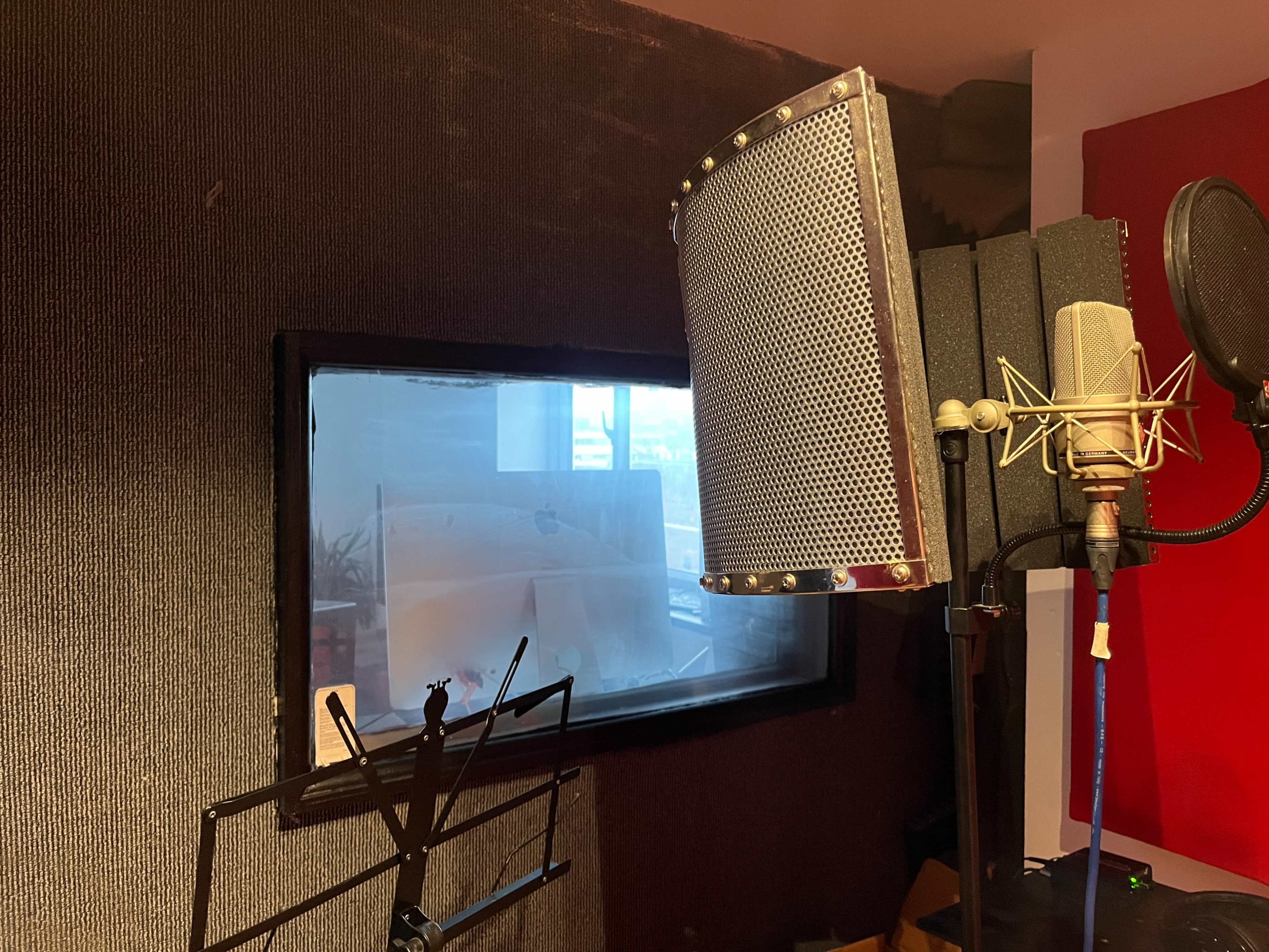 A recording studio setup with a microphone and a soundproof window.