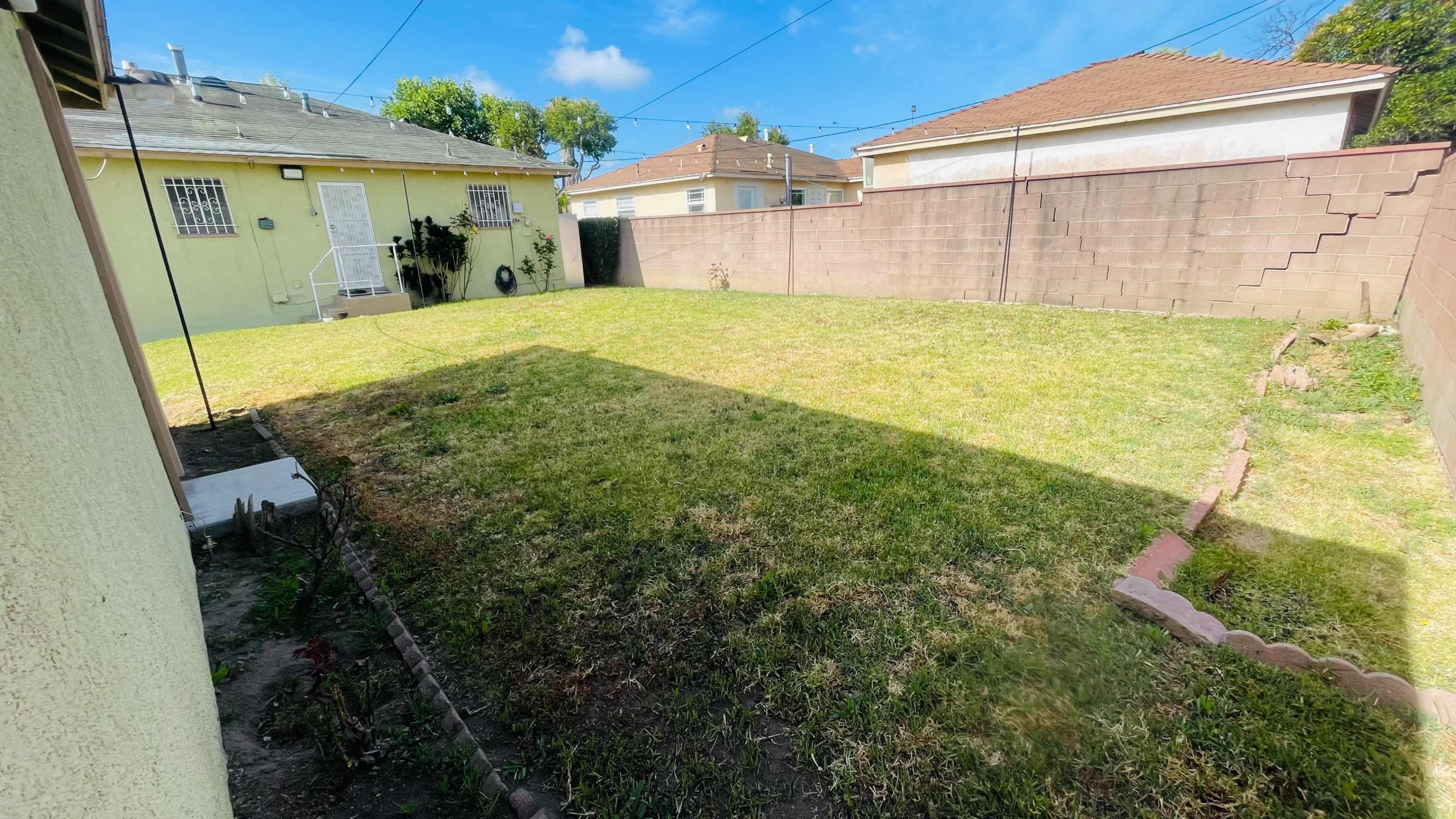 The image shows a grassy backyard bordered by a fence and two houses, with a clear blue sky overhead.