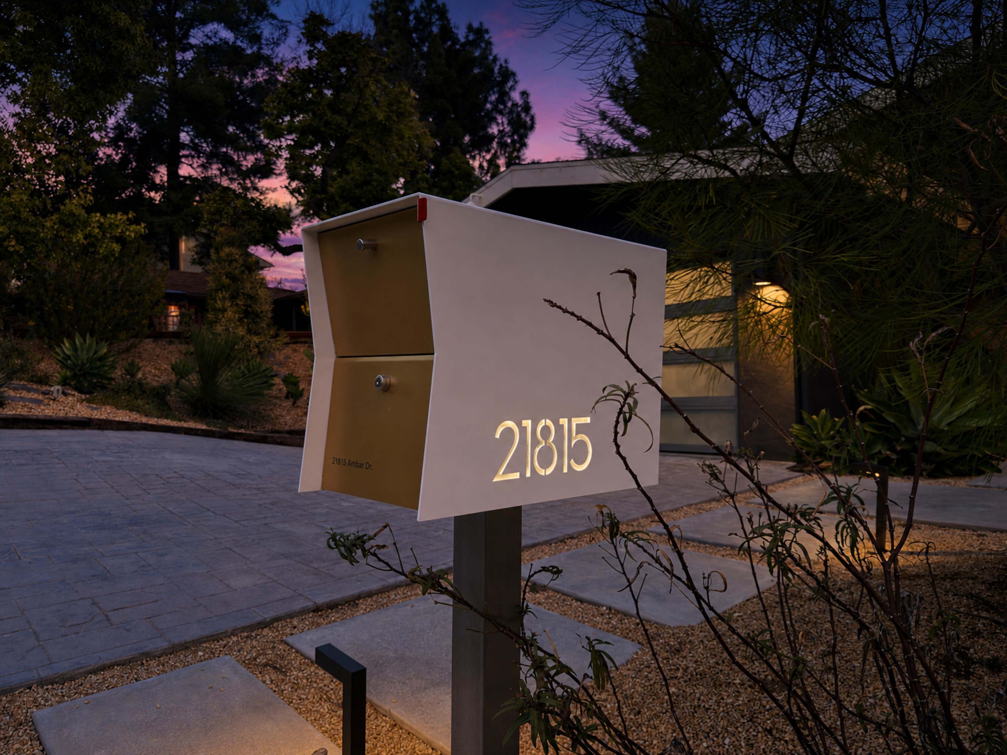 The image shows a modern mailbox with the number "21815" illuminated, positioned in a landscaped yard at dusk.