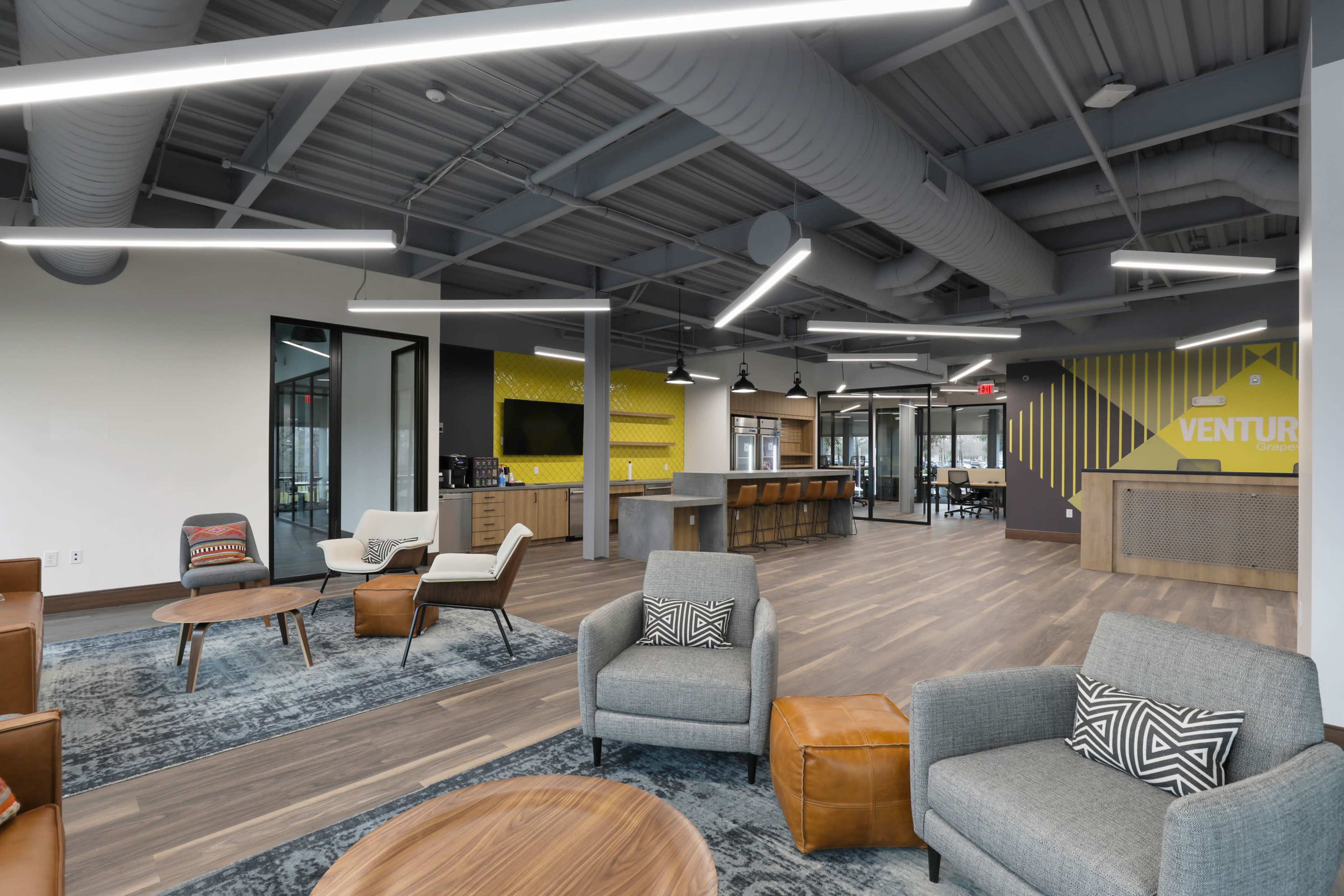 A modern office space with a reception area, meeting rooms, and seating arrangements featuring various furniture styles and a large wall displaying the word "VENTURE."