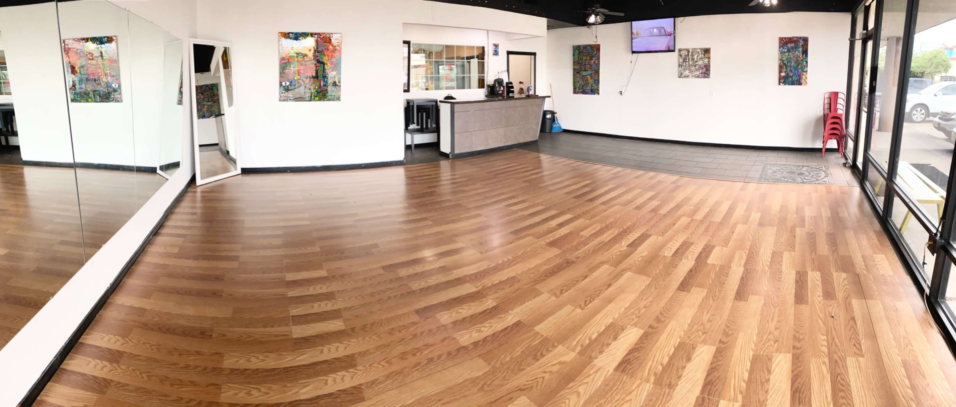 A spacious interior of a studio with wooden flooring, mirrors on one wall, and artwork mounted on the walls.