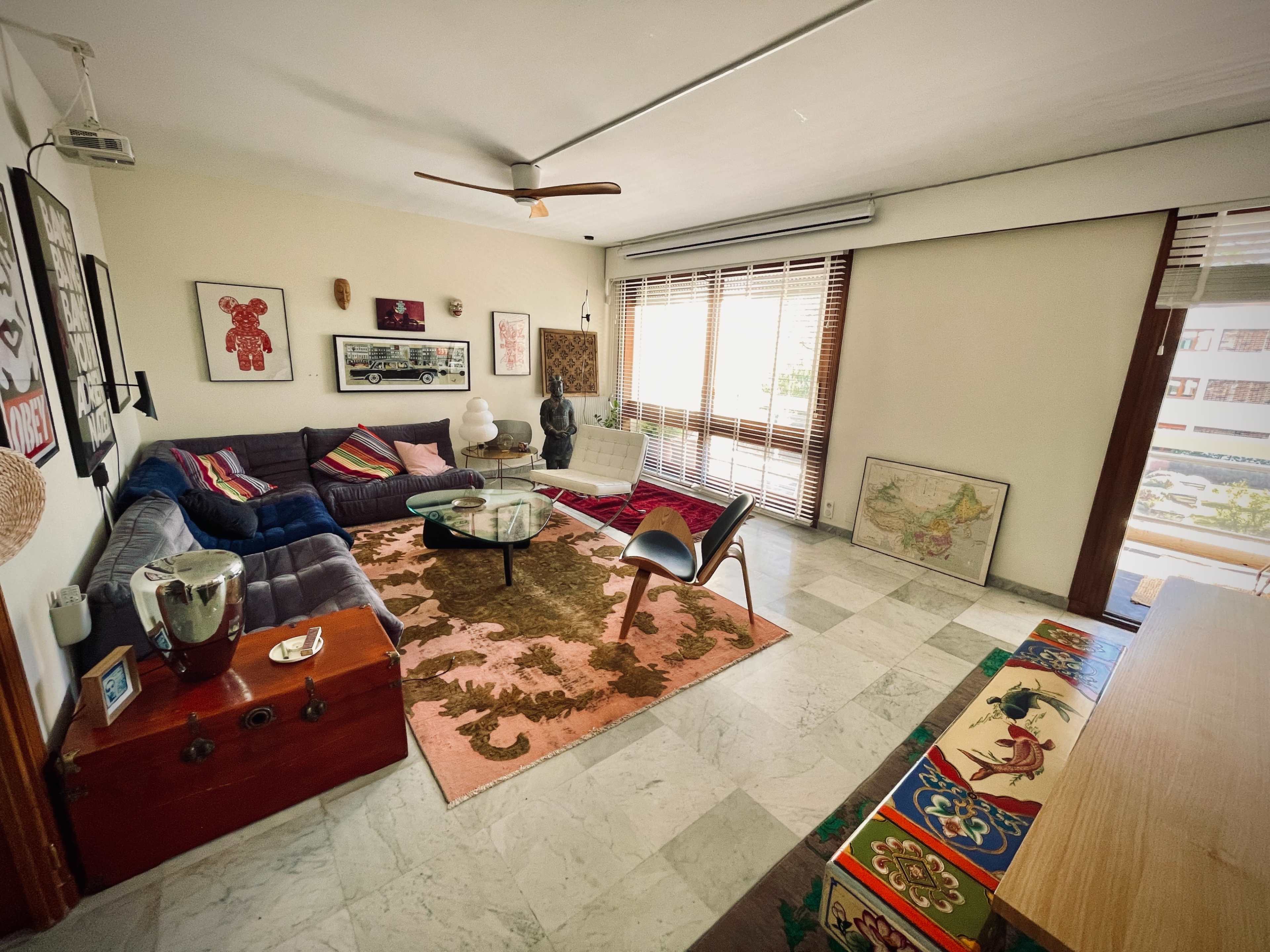 The living room features a mix of modern and vintage furniture, a large rug, and large windows allowing natural light to enter.