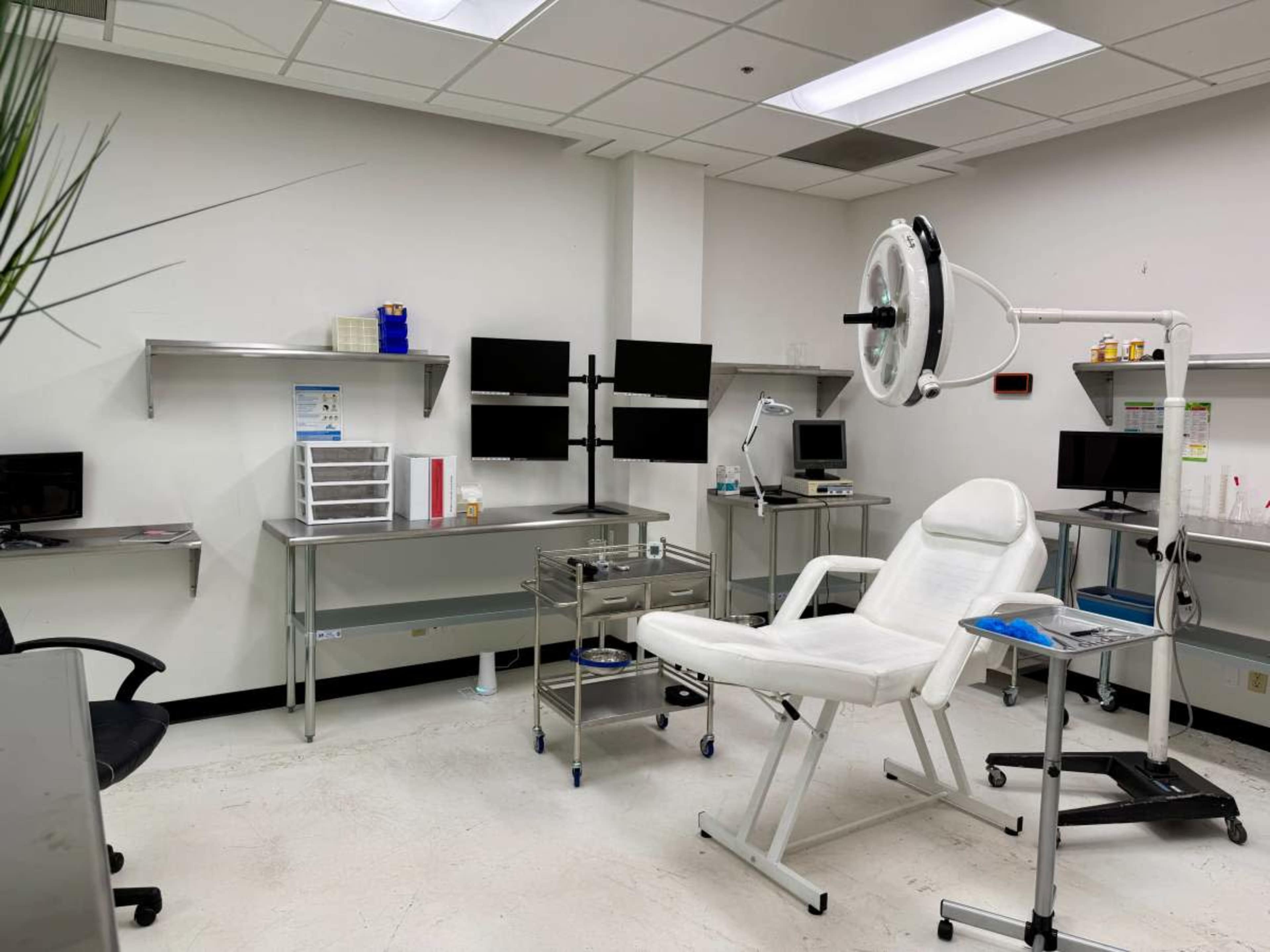 The image shows a medical examination room equipped with a treatment chair, various workstations, and several medical instruments.