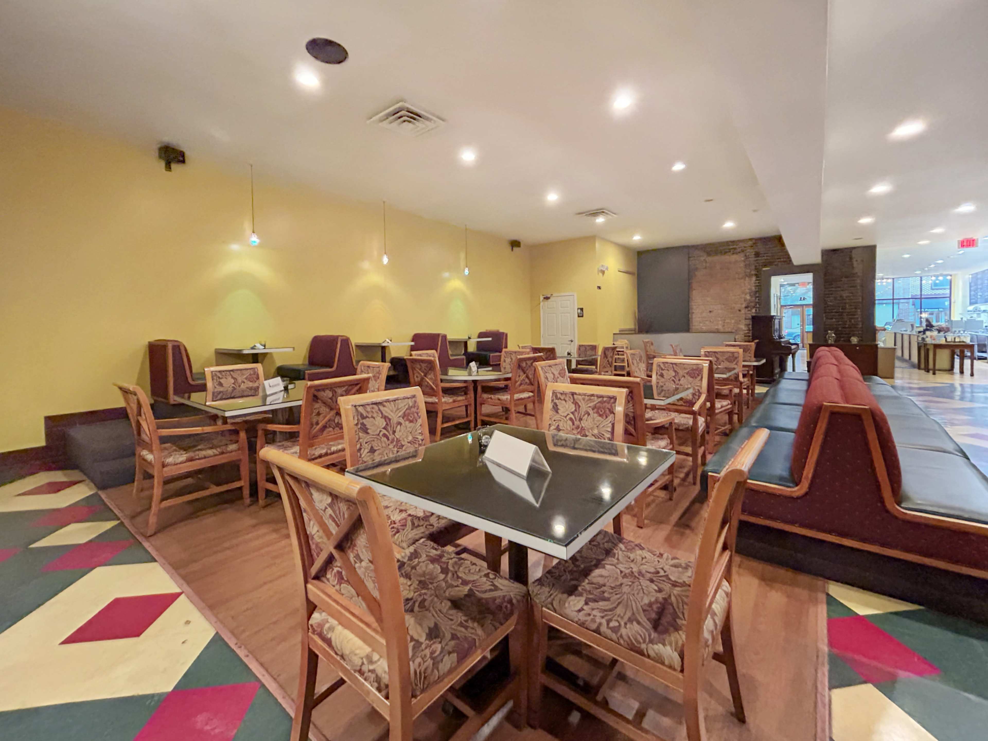 A dining area with wooden tables and chairs, featuring a mix of seating types in a space decorated with yellow walls and patterned flooring.