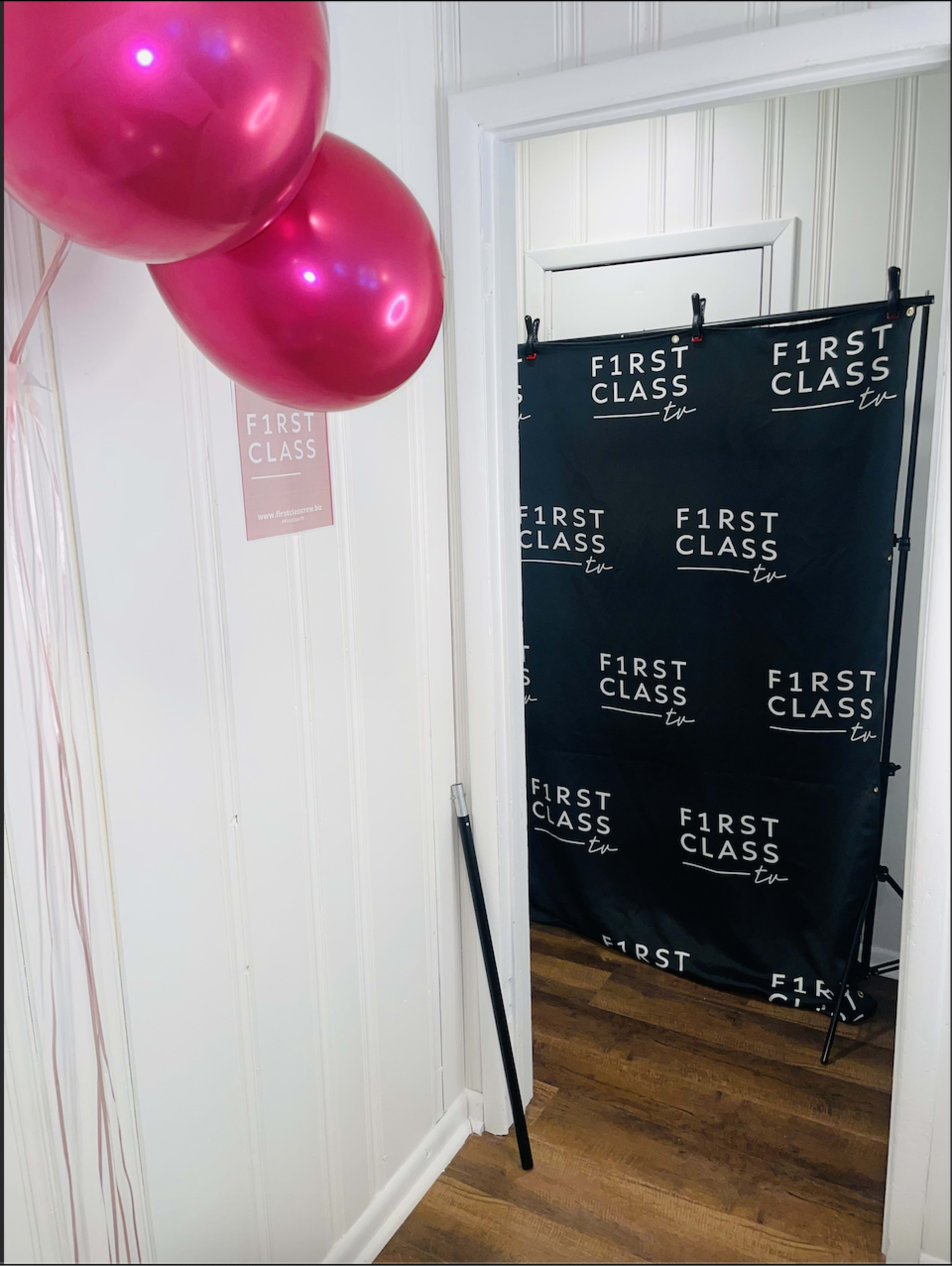 An entrance with pink balloons and a black backdrop featuring the text "F1RST CLASS" in white.
