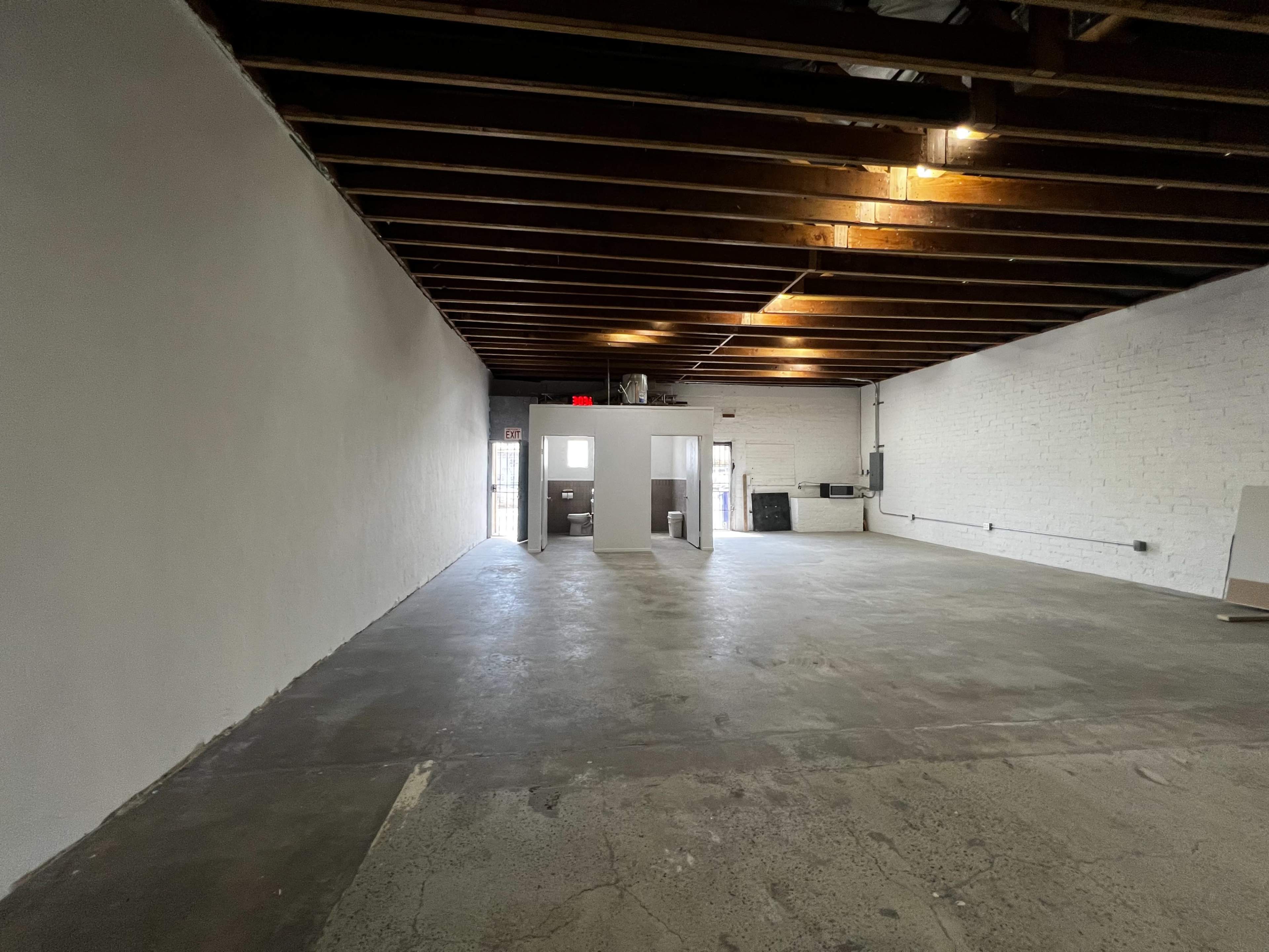 A spacious, unfinished interior of a commercial building with exposed wooden beams and a concrete floor.