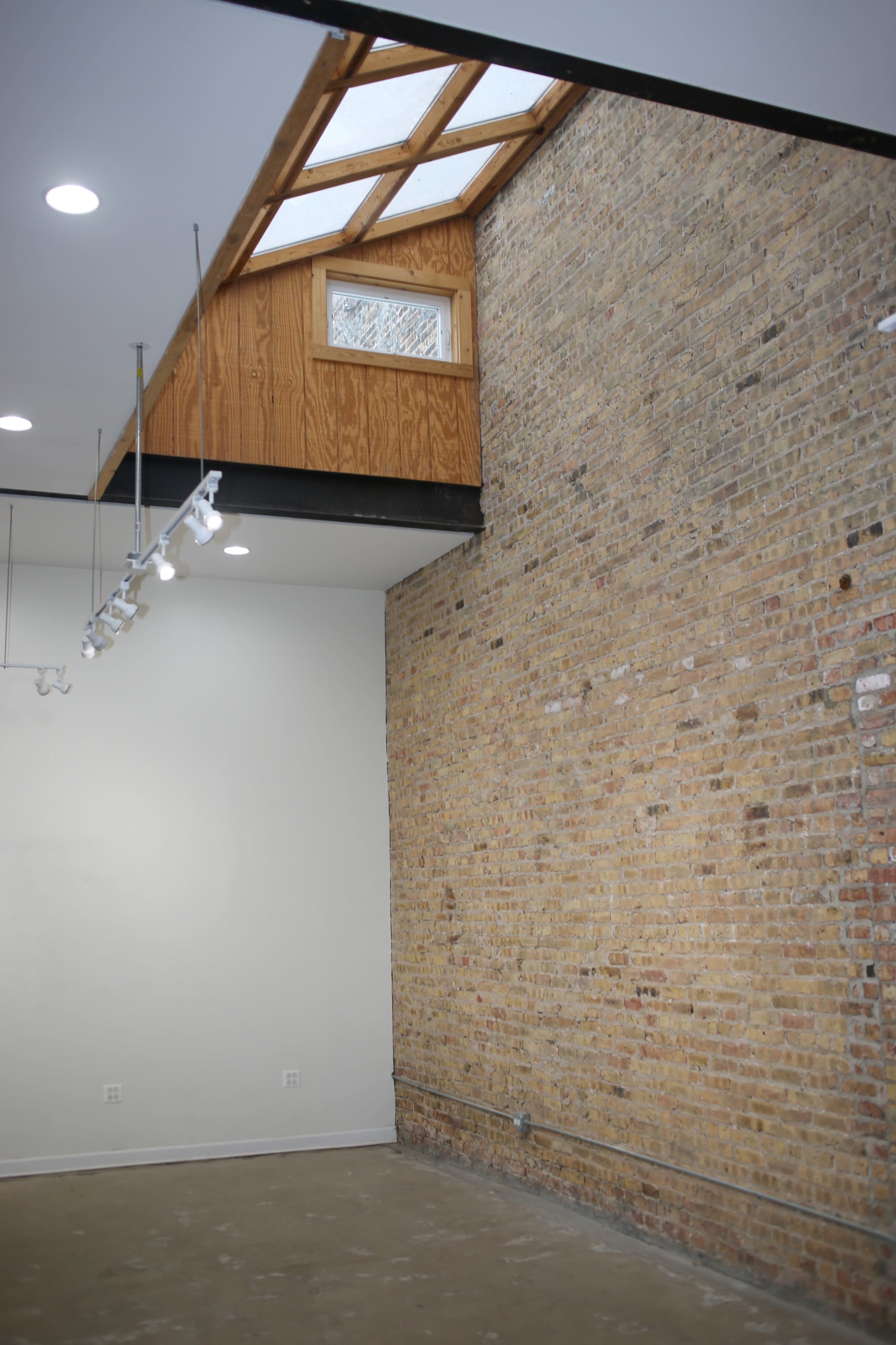 The image shows an interior space with a brick wall, a wooden loft structure at the top, and modern lighting fixtures.