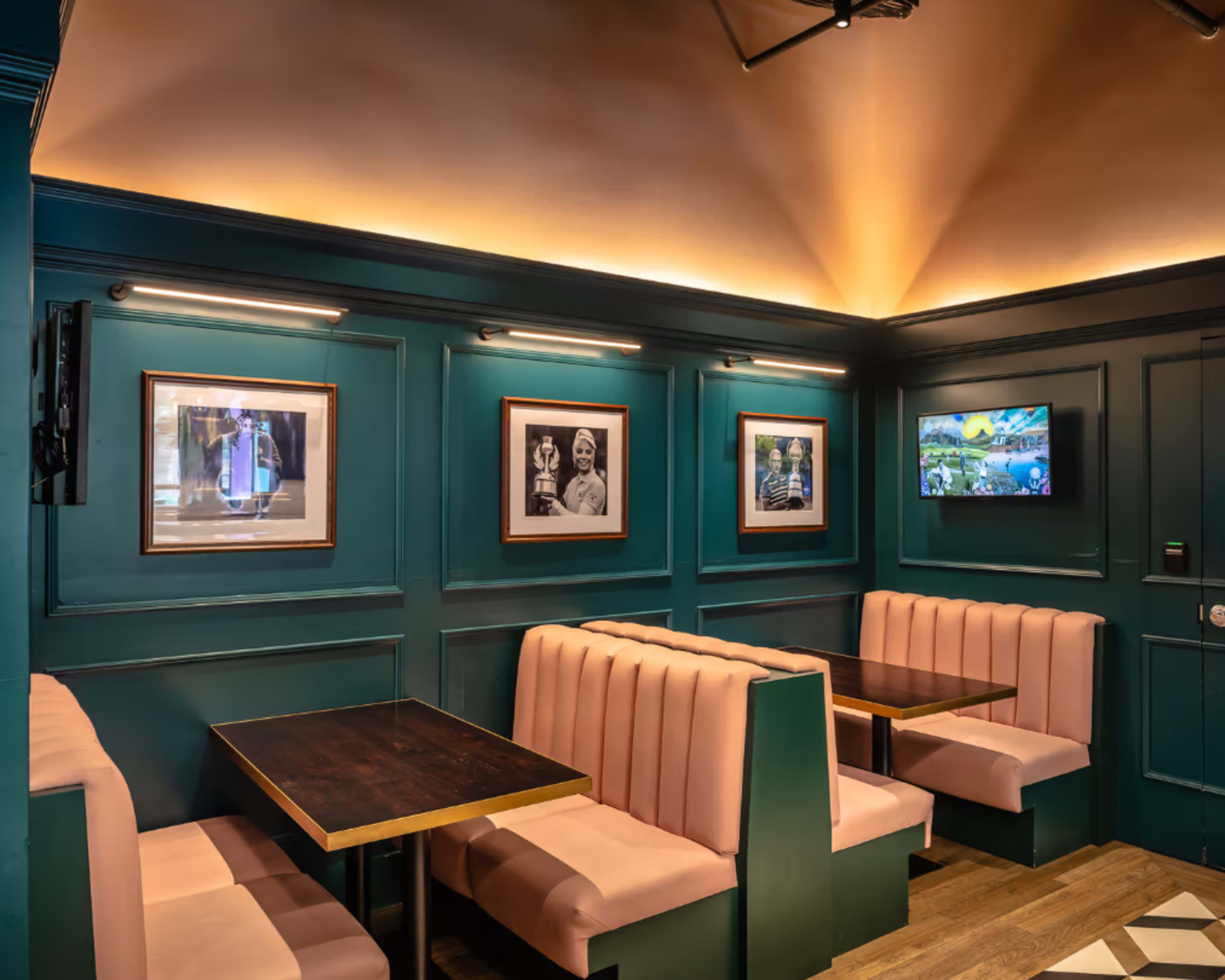 The image shows a cozy restaurant interior with teal walls, pink upholstered seating, framed pictures, and a television mounted on the wall.