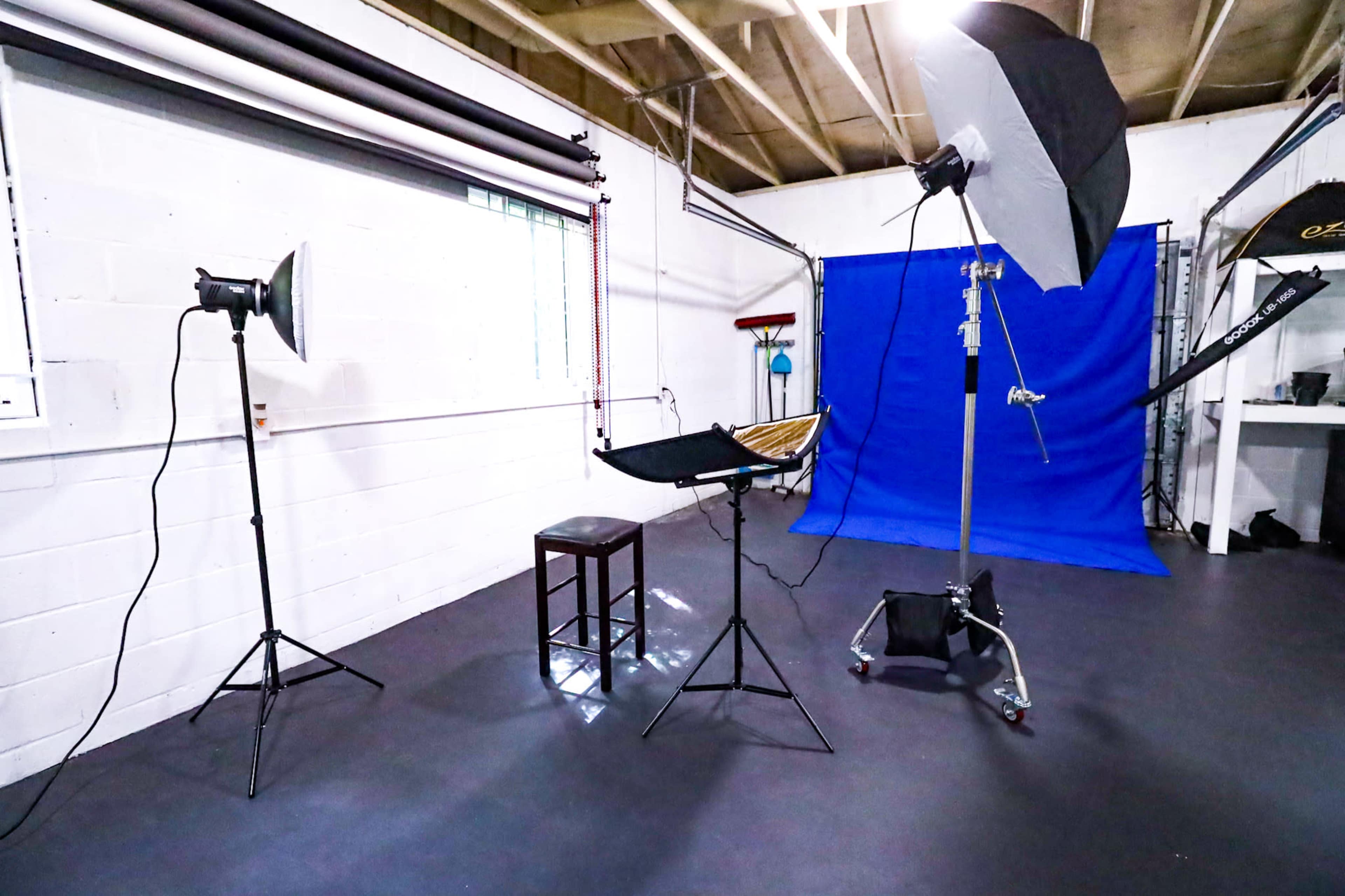A photography studio with lighting equipment, a stool, and a blue backdrop.