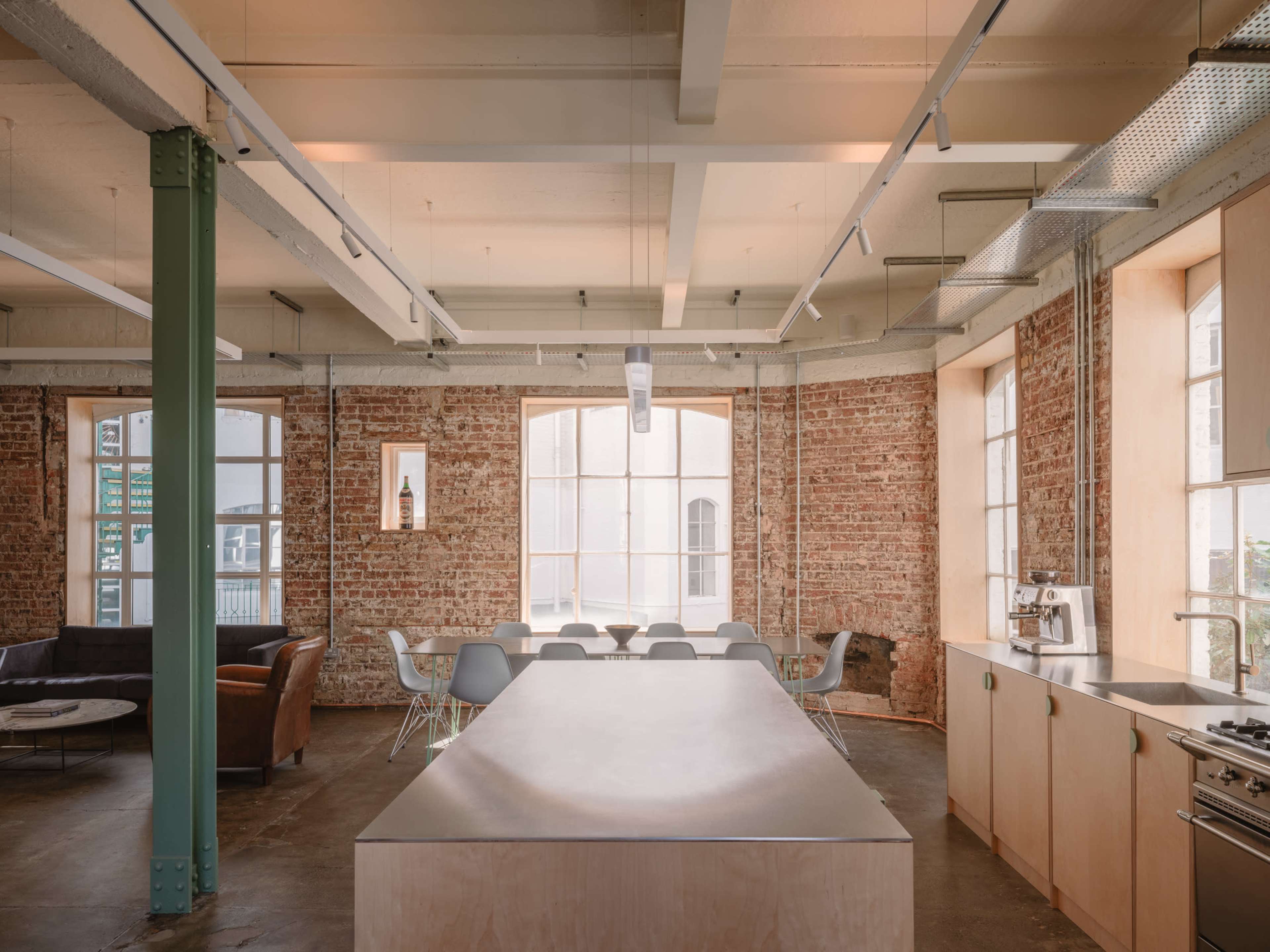 The image shows a modern kitchen and dining area with exposed brick walls, a long counter, and a mixture of seating options.