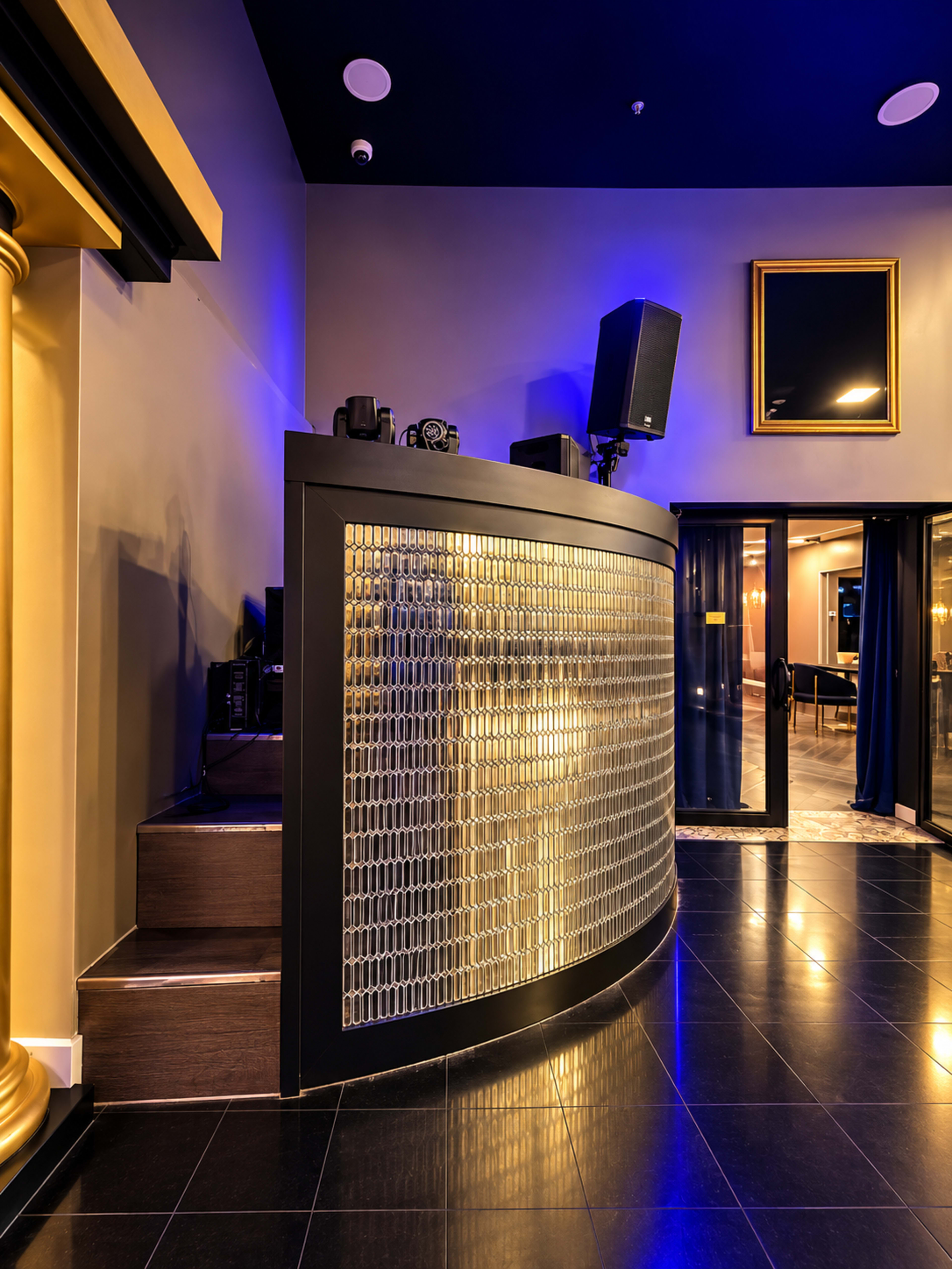 The image shows a modern, stylish bar area with a curved backlit counter and audio equipment in a dimly lit venue.