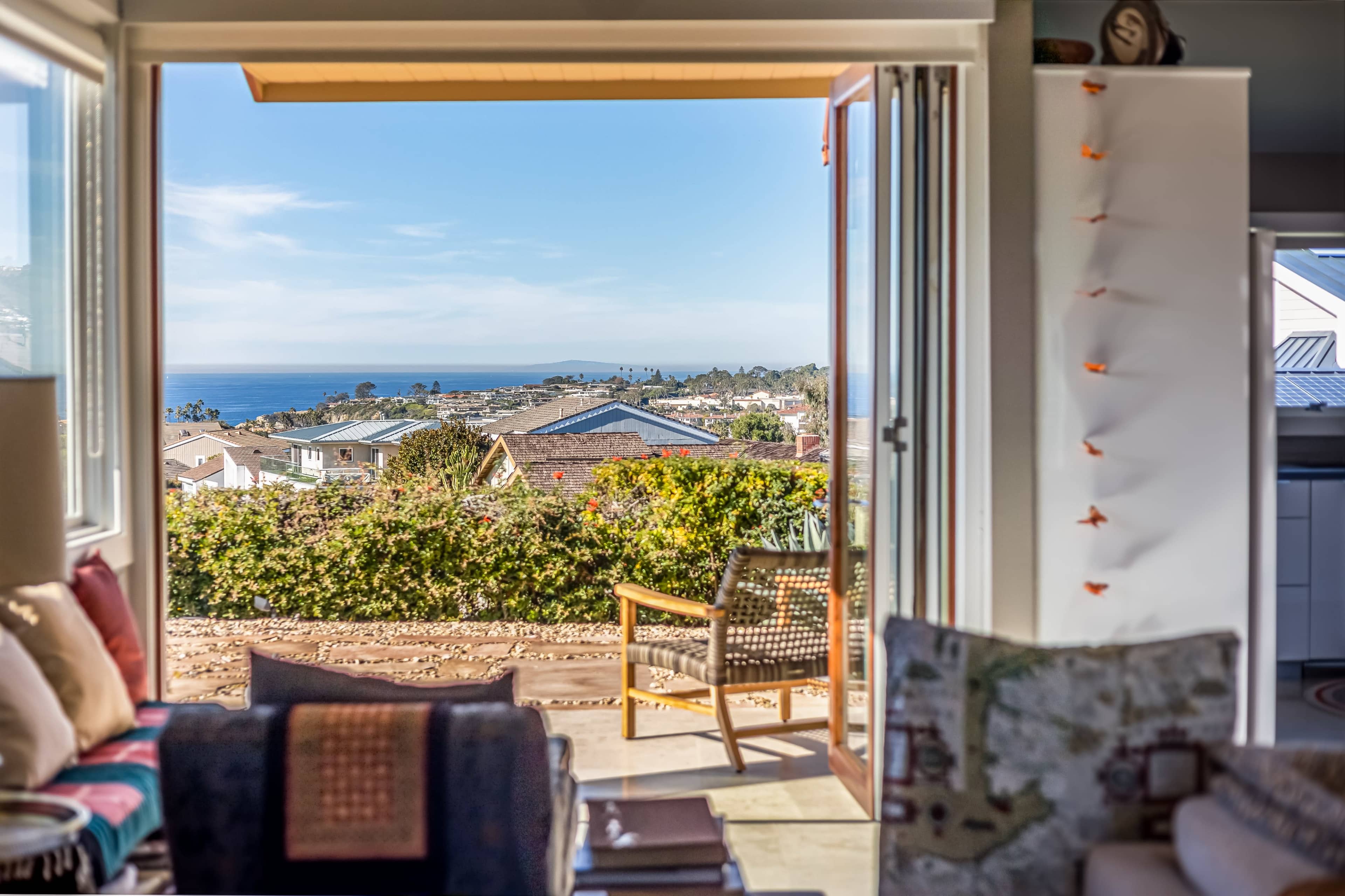 A cozy living room opens to a view of the ocean and surrounding homes through sliding glass doors.