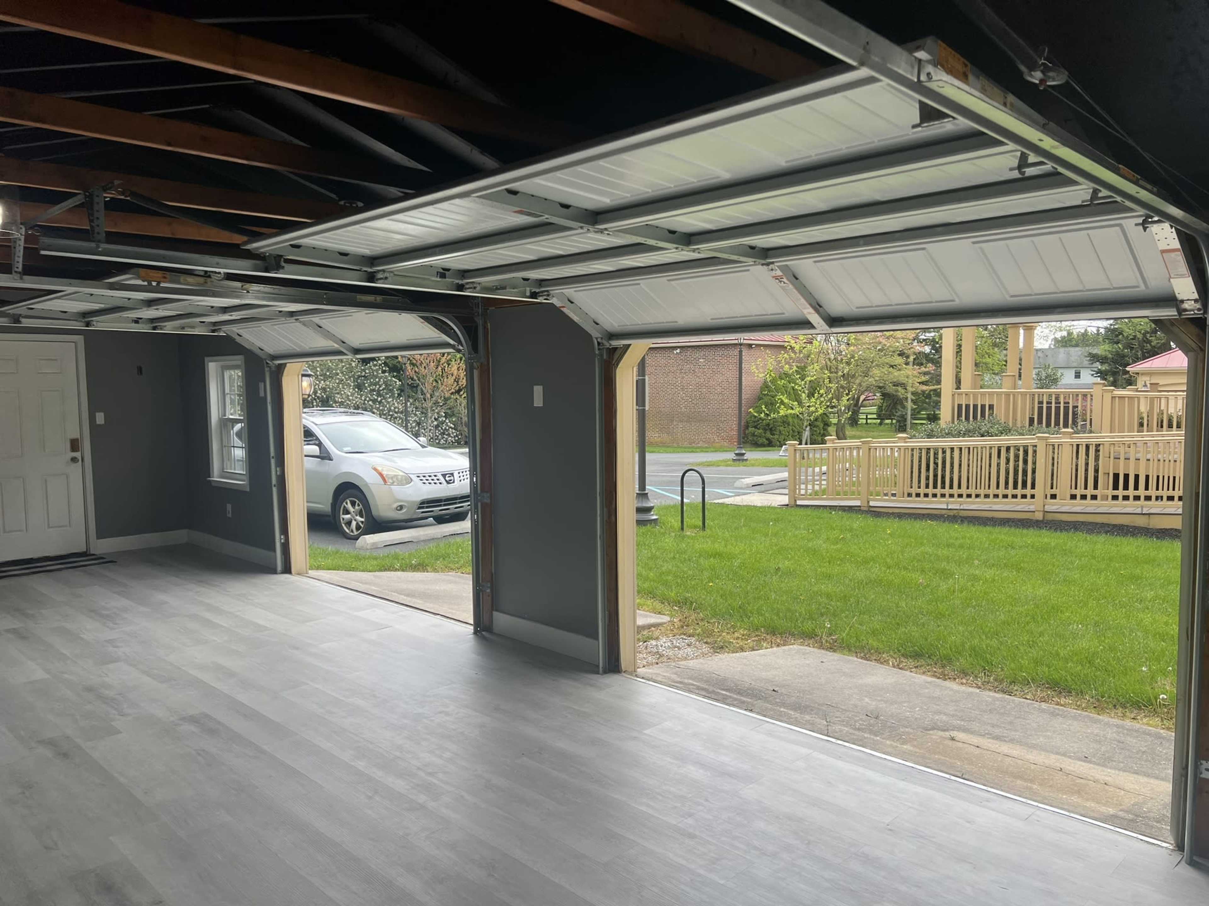 An empty garage with two open doors, revealing a view of the outside lawn and a paved area.