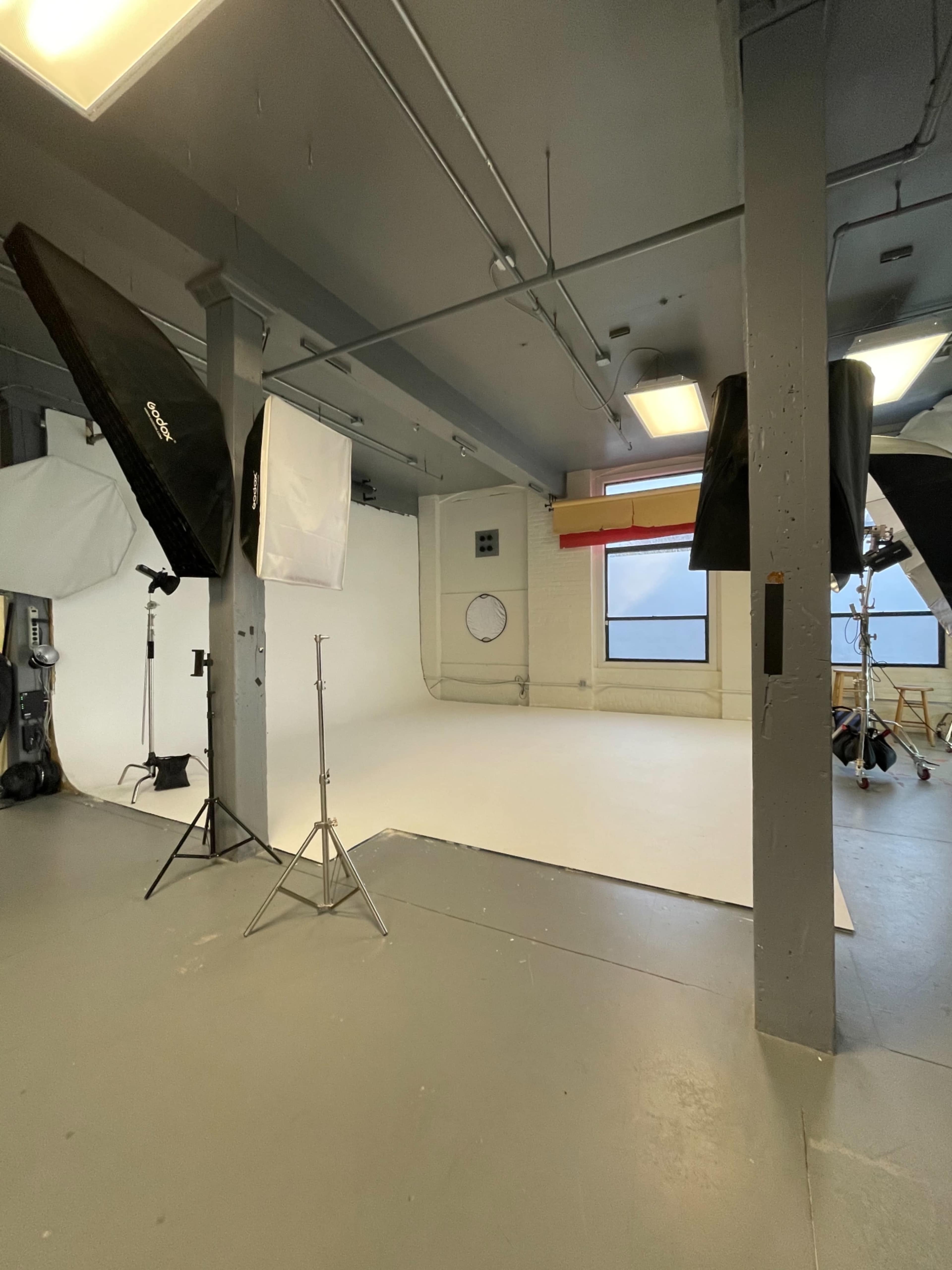 A photography studio with softbox lights and a white backdrop set up for a photoshoot.