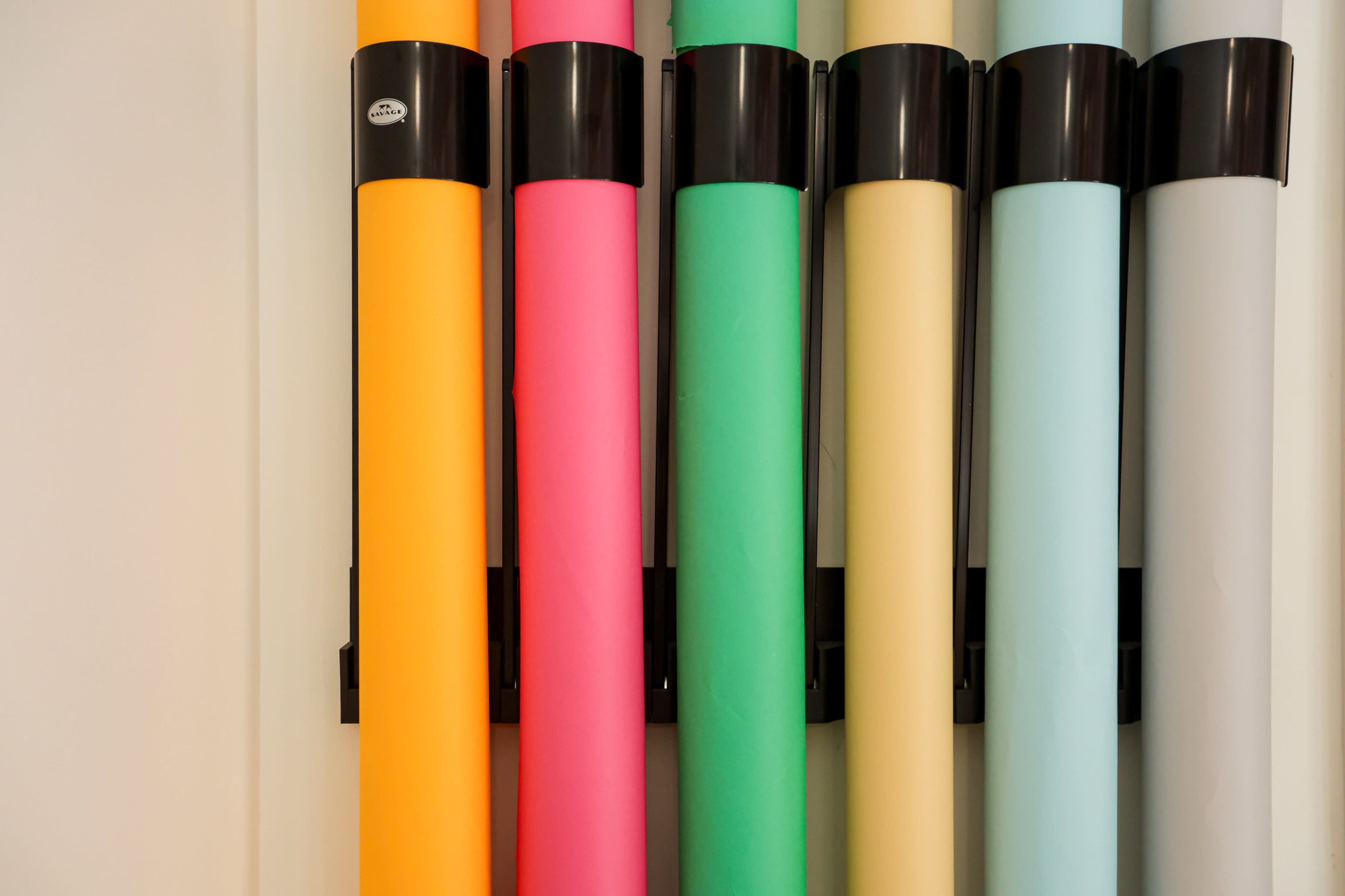 Colorful rolls of paper are mounted vertically on a black holder against a white wall.