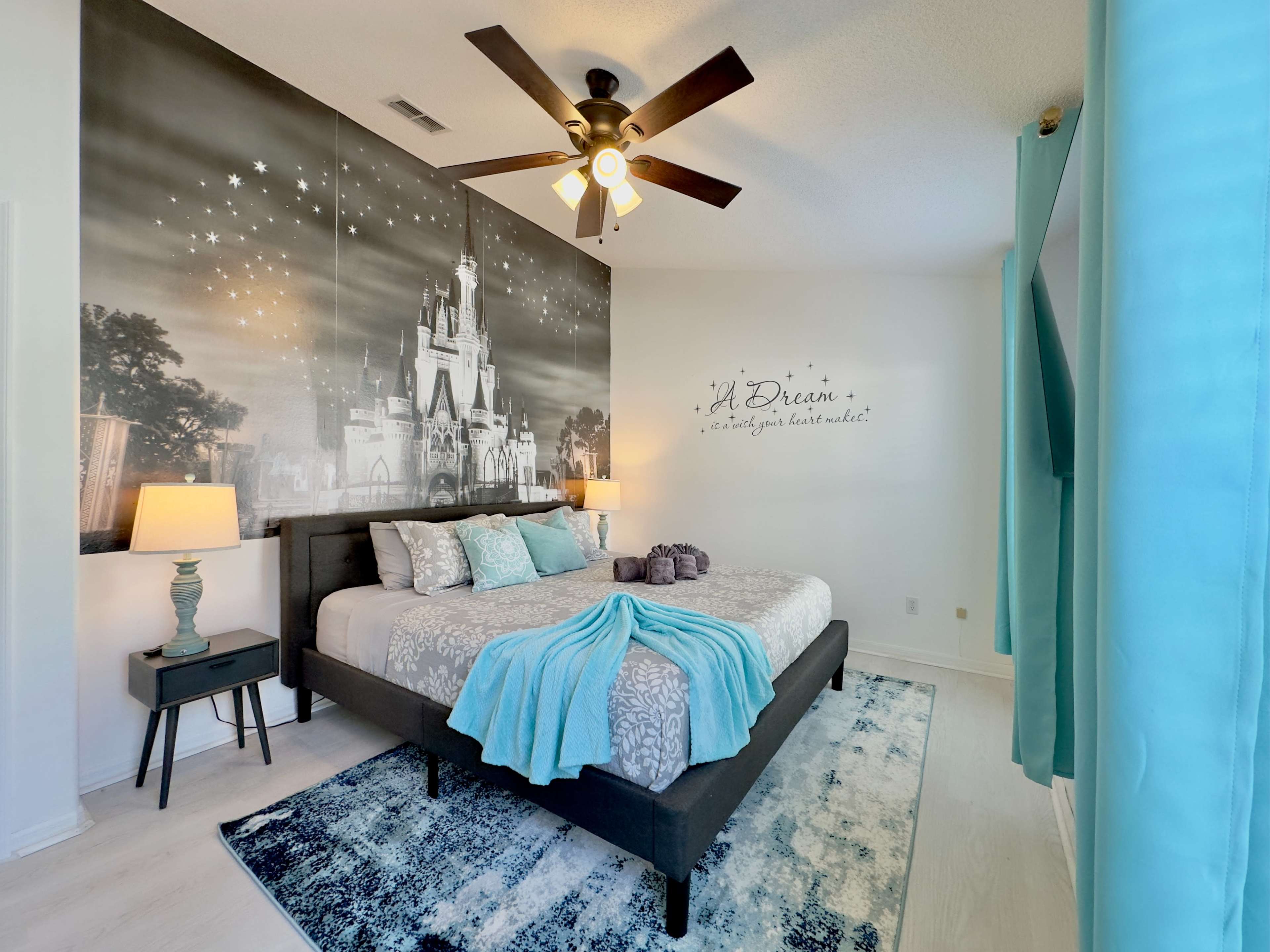 The room features a bed with a light blue throw blanket and a large mural of a castle on the wall, accompanied by two bedside lamps and curtains.