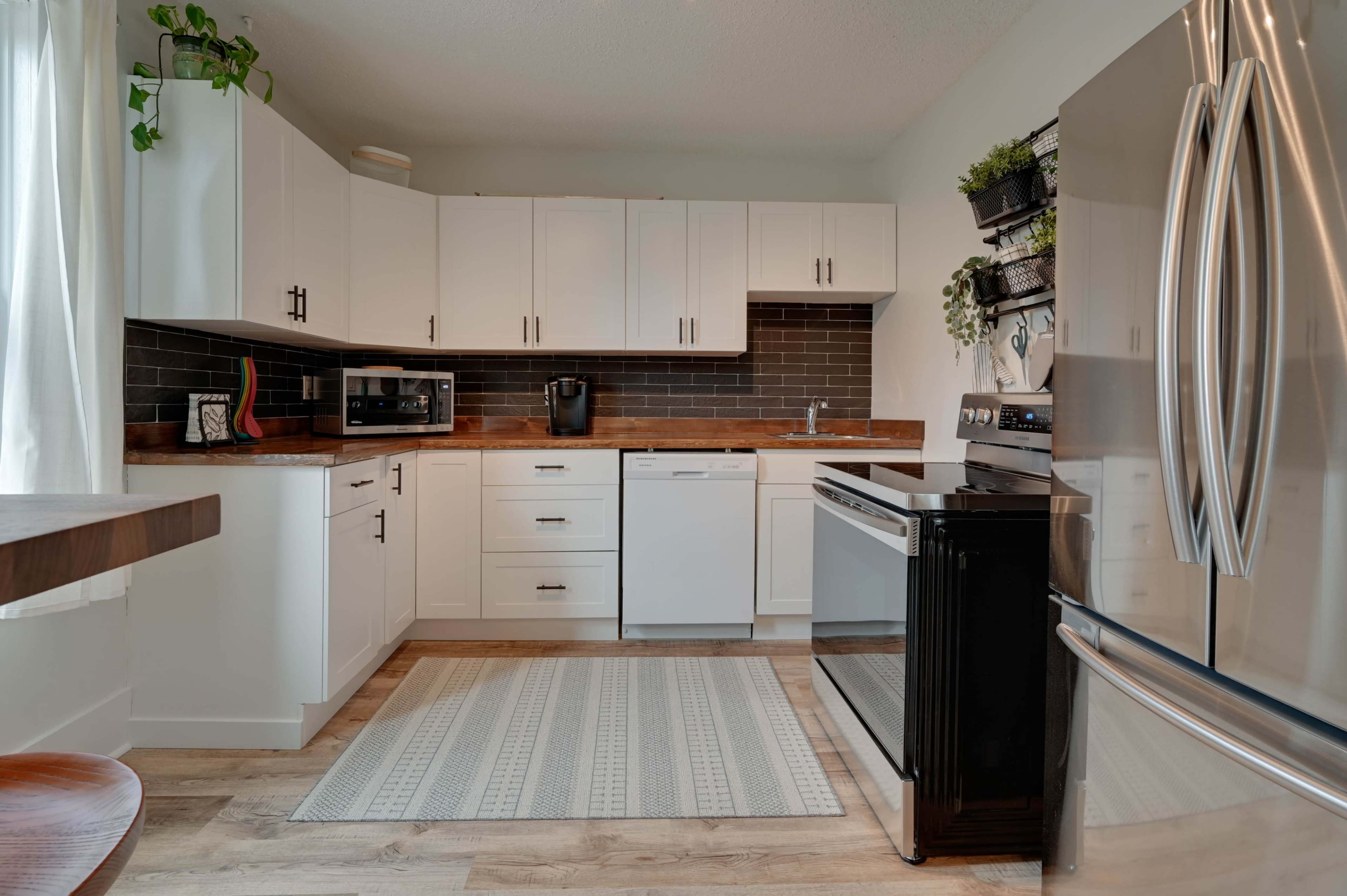 A modern kitchen features white cabinetry, stainless steel appliances, and a dark backsplash, with a rug positioned on a wooden floor.