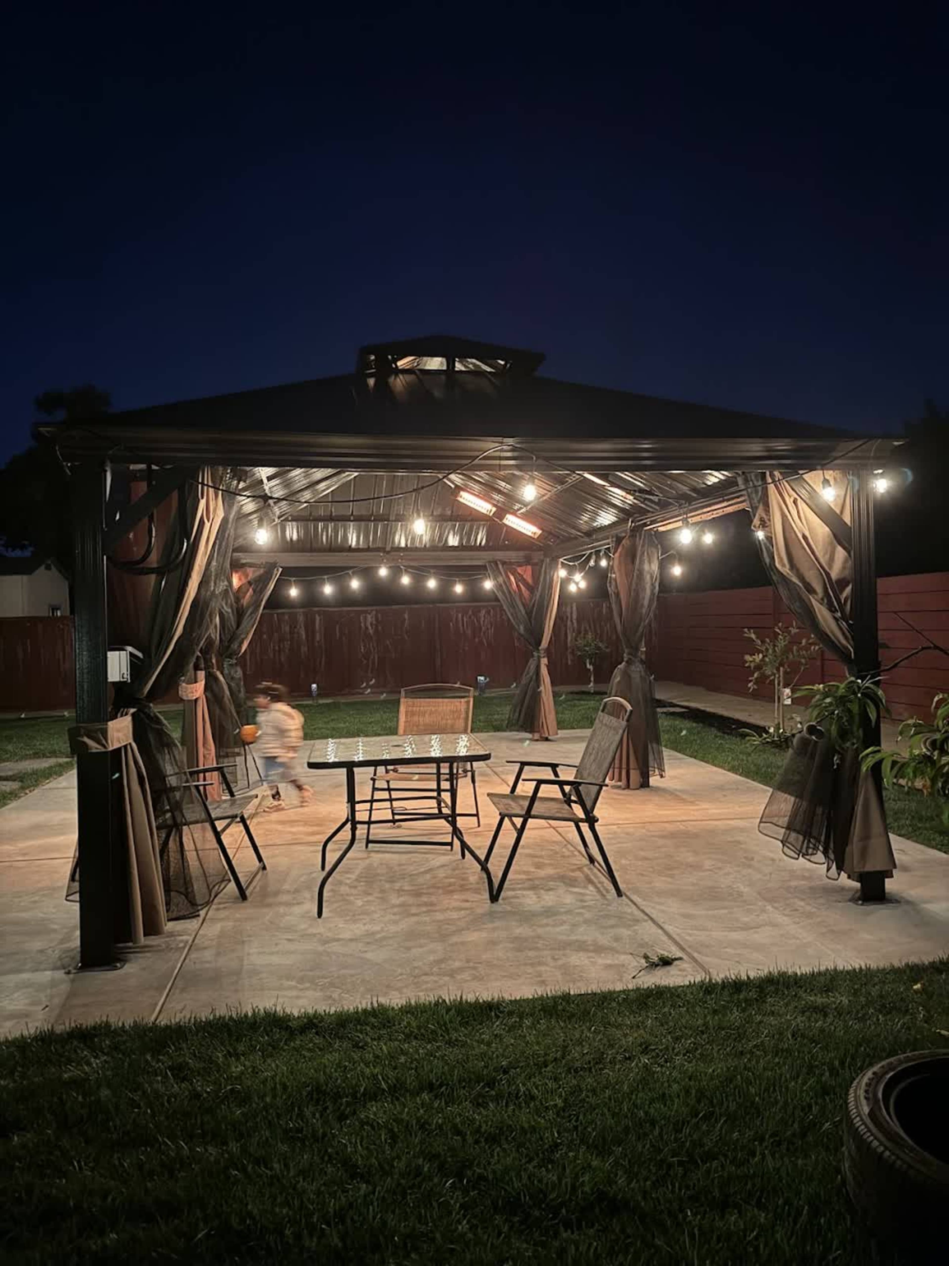 A gazebo with string lights is surrounded by chairs and is set against a dark night sky.