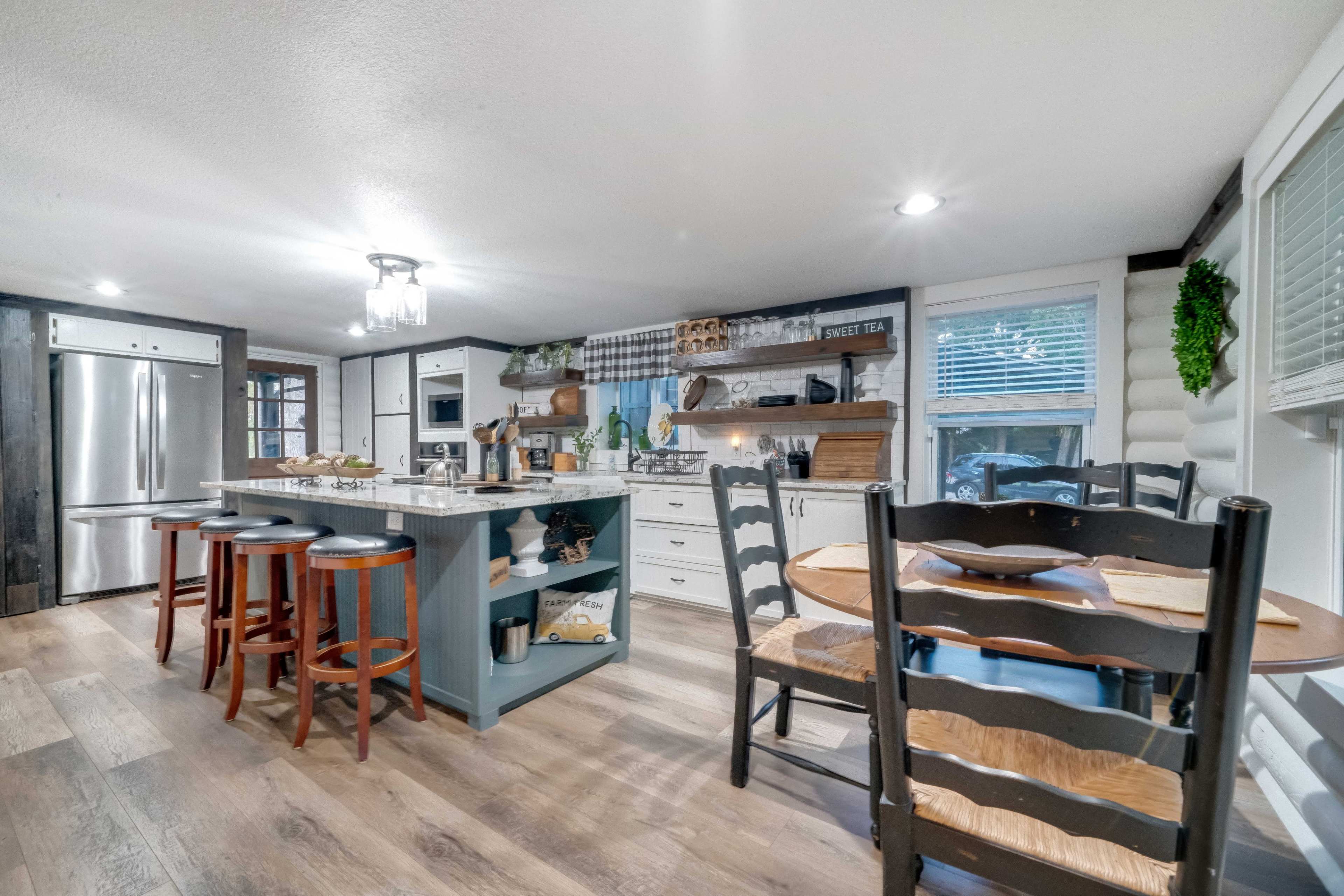 The image shows a modern kitchen with a central island, bar seating, and a dining area featuring a table and chairs.