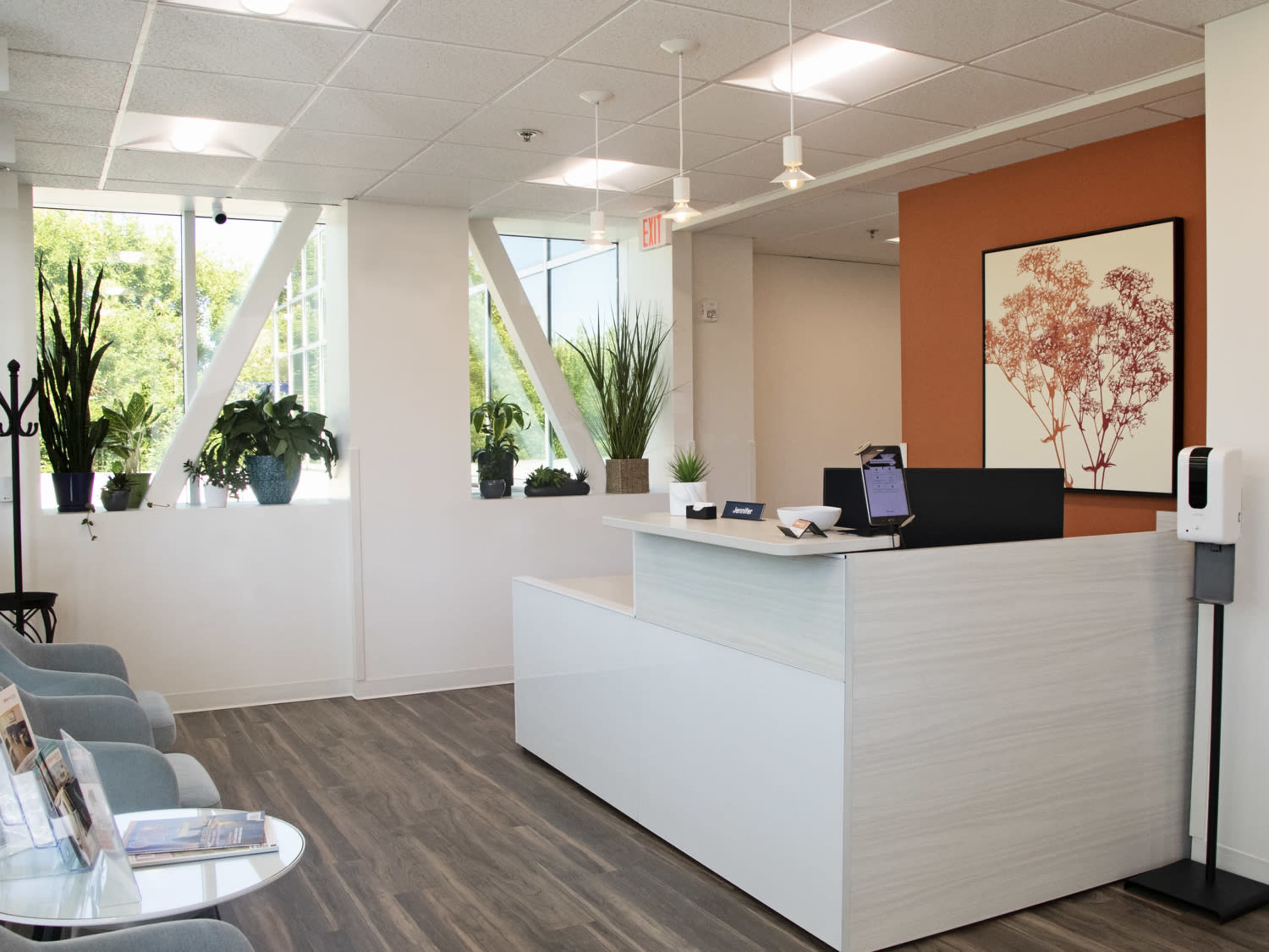A modern reception area with a desk, seating, and various potted plants.