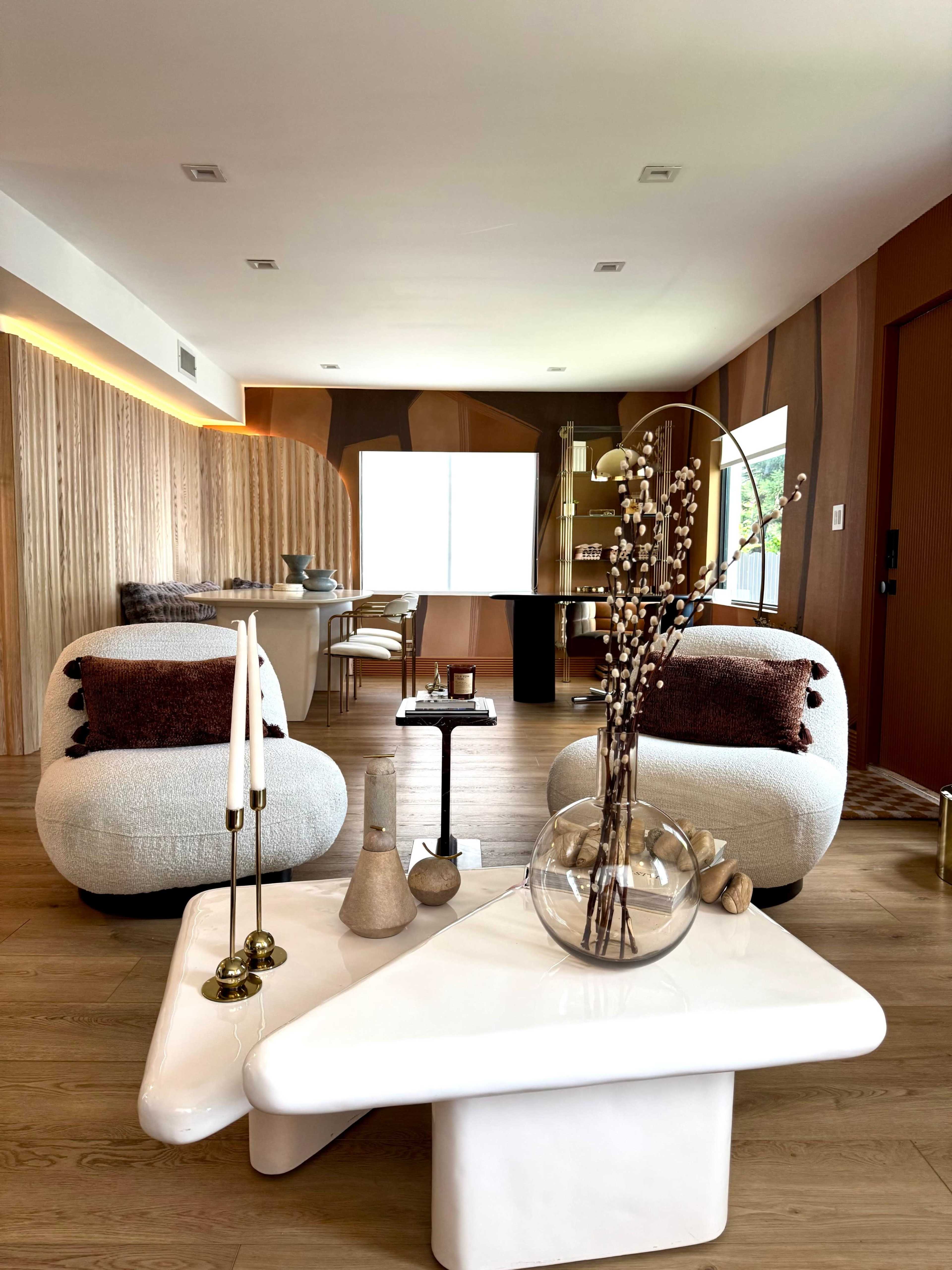 The image shows a modern living room featuring two plush armchairs, a unique coffee table with decorative items, and a dining area in the background.