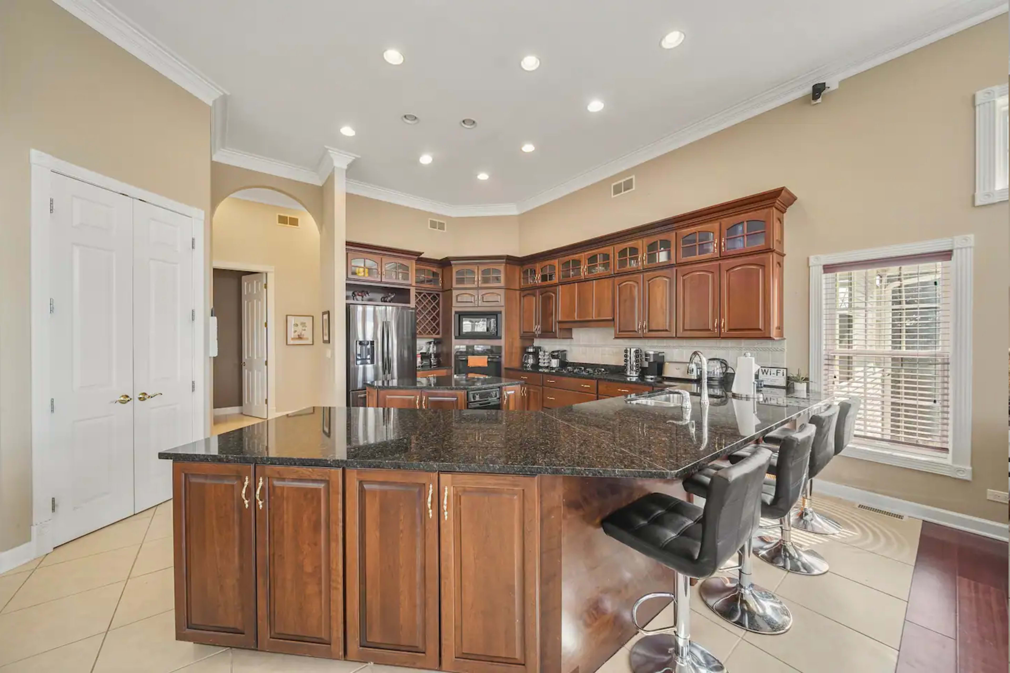 A modern kitchen featuring dark wood cabinets, a large granite island with bar stools, and stainless steel appliances.
