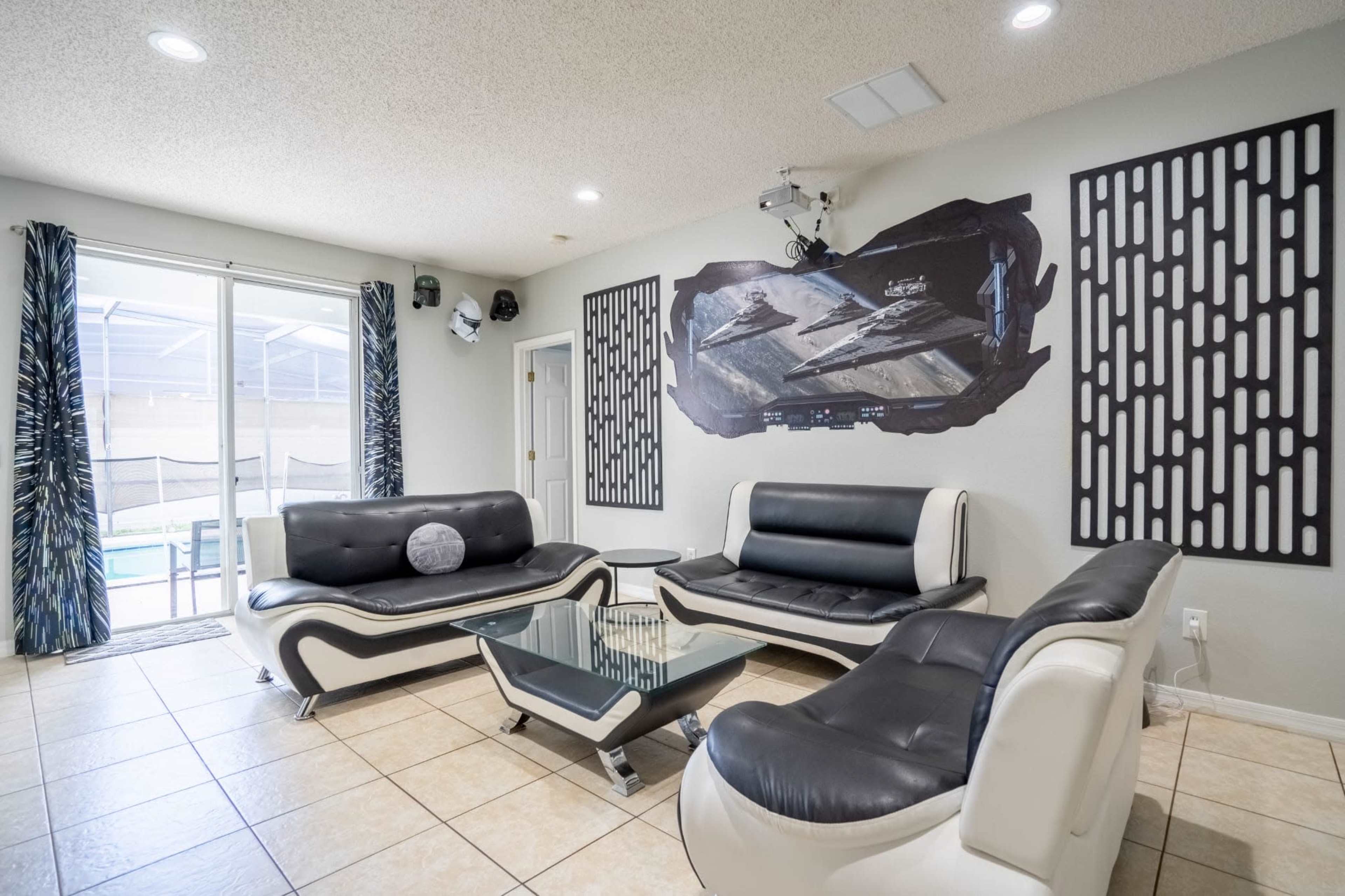 The living room features modern black and white furniture, a glass coffee table, and a large wall mural depicting a space scene.