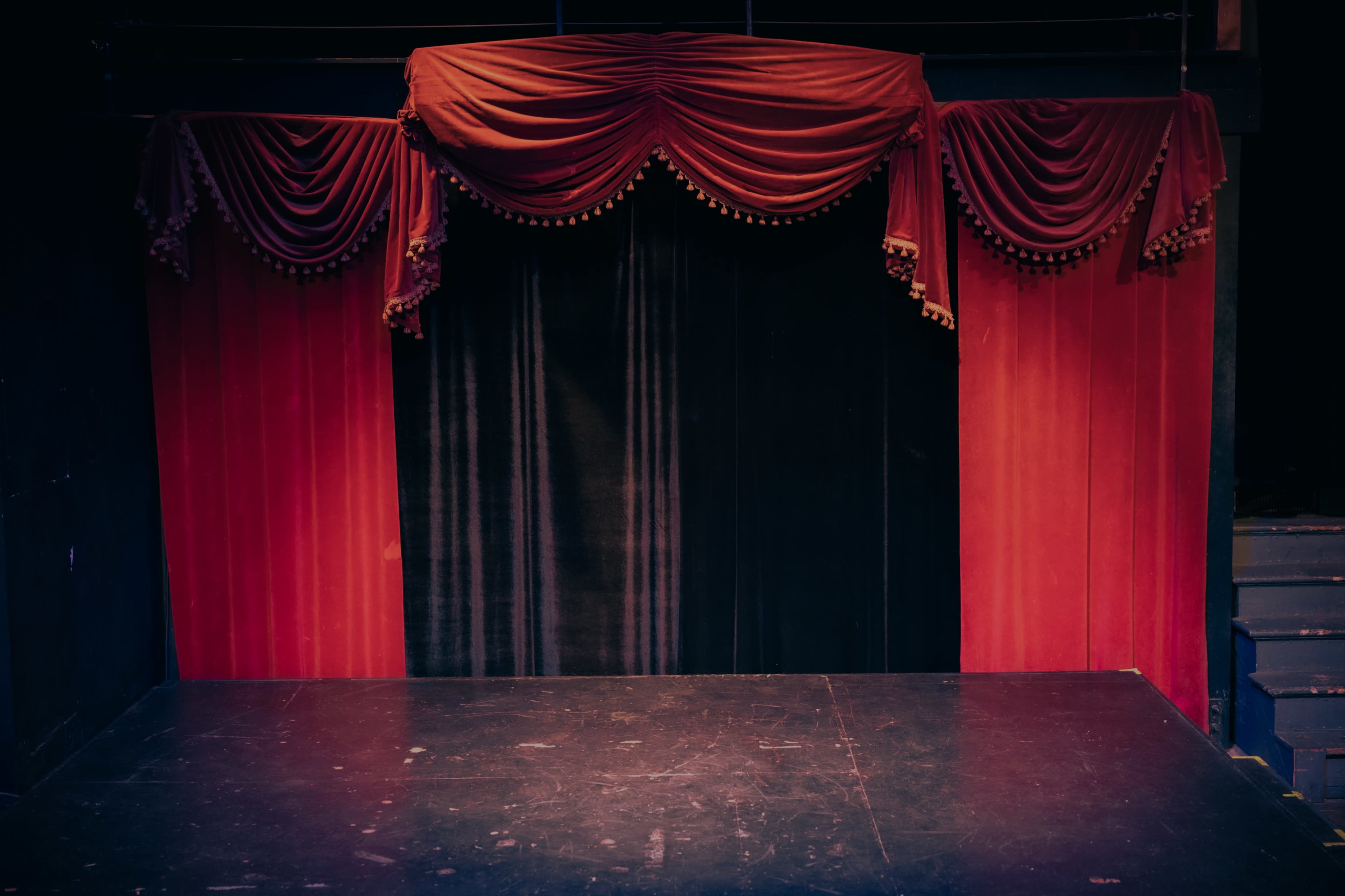 A stage with a red and black curtain draped above a dark floor.