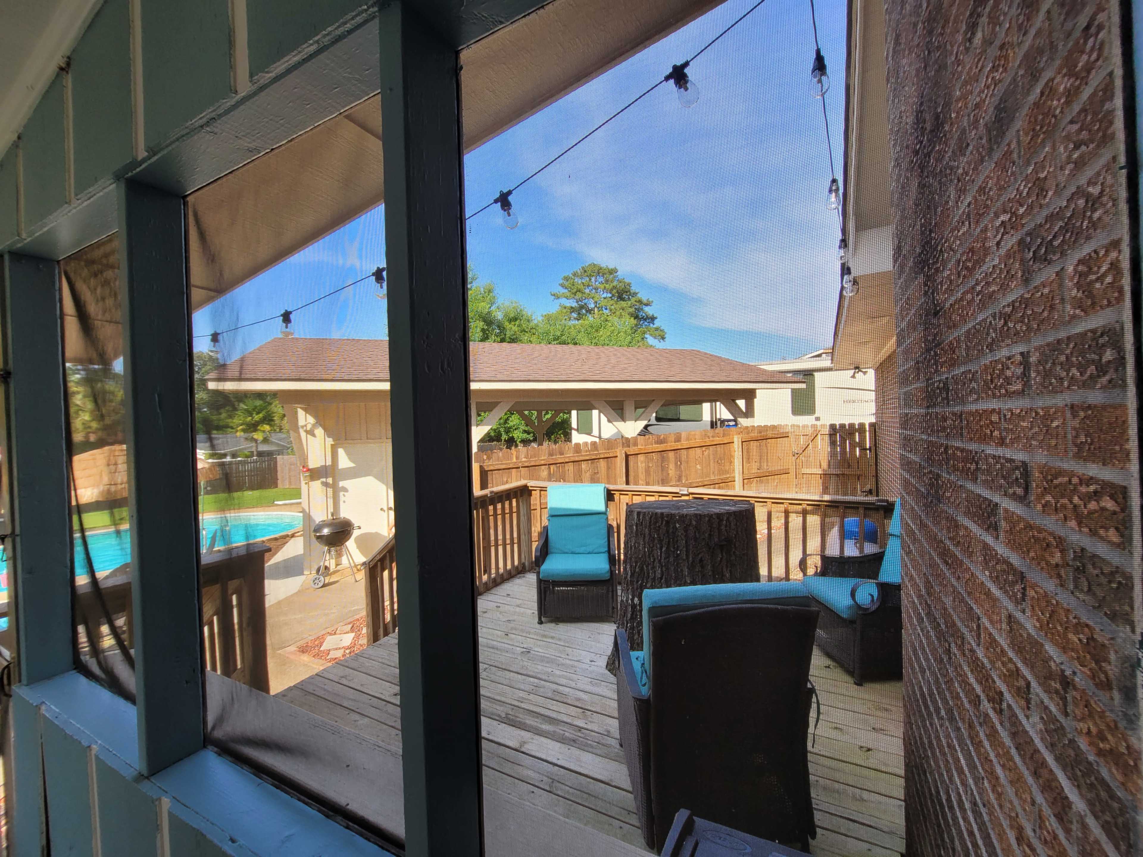 A wooden deck is visible through a screened window, featuring patio furniture and a view of a pool and surrounding yard.