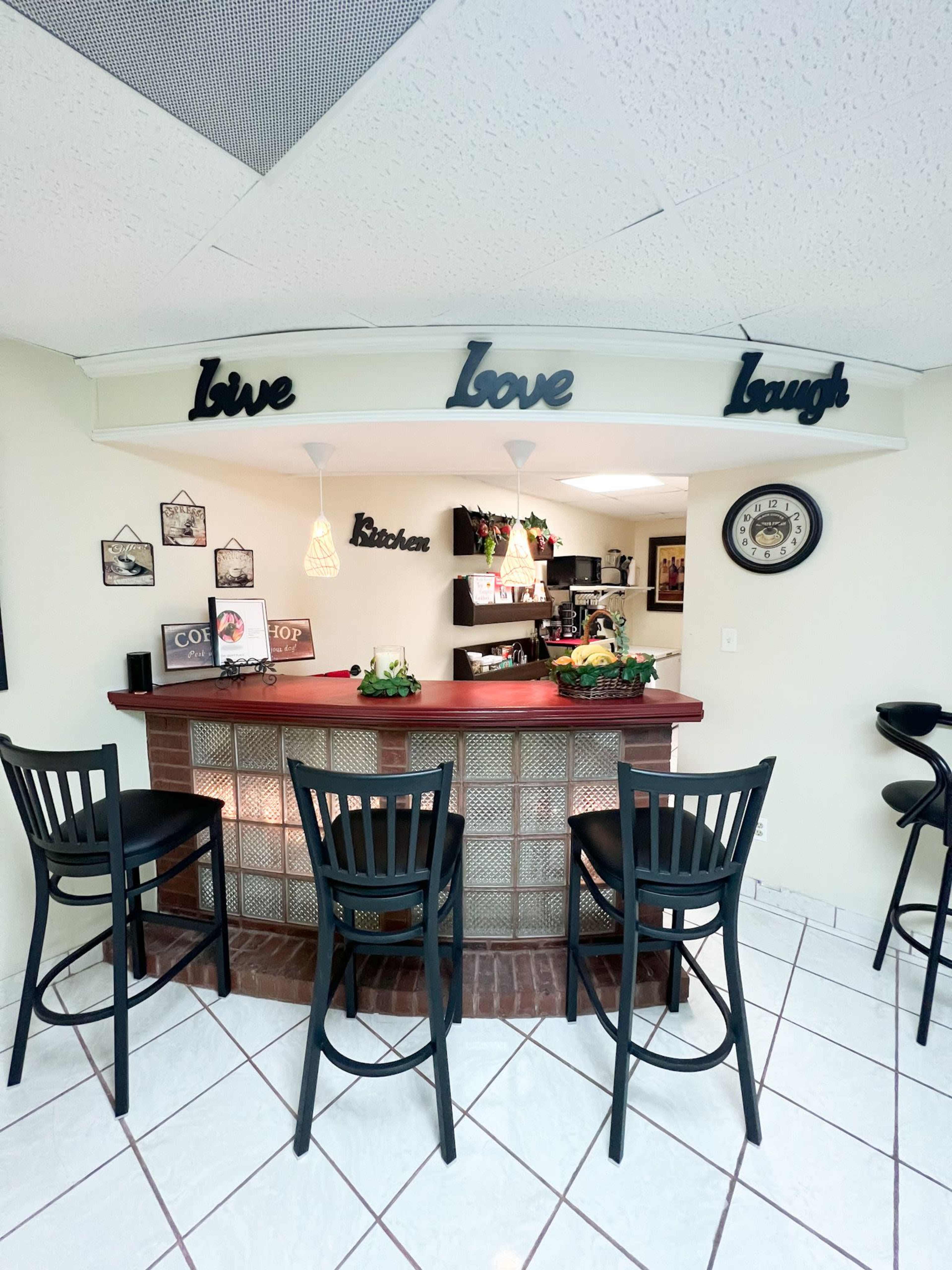 A small kitchen bar area features a red countertop with black stools and decorative signs reading "Love Love Laugh" above it.