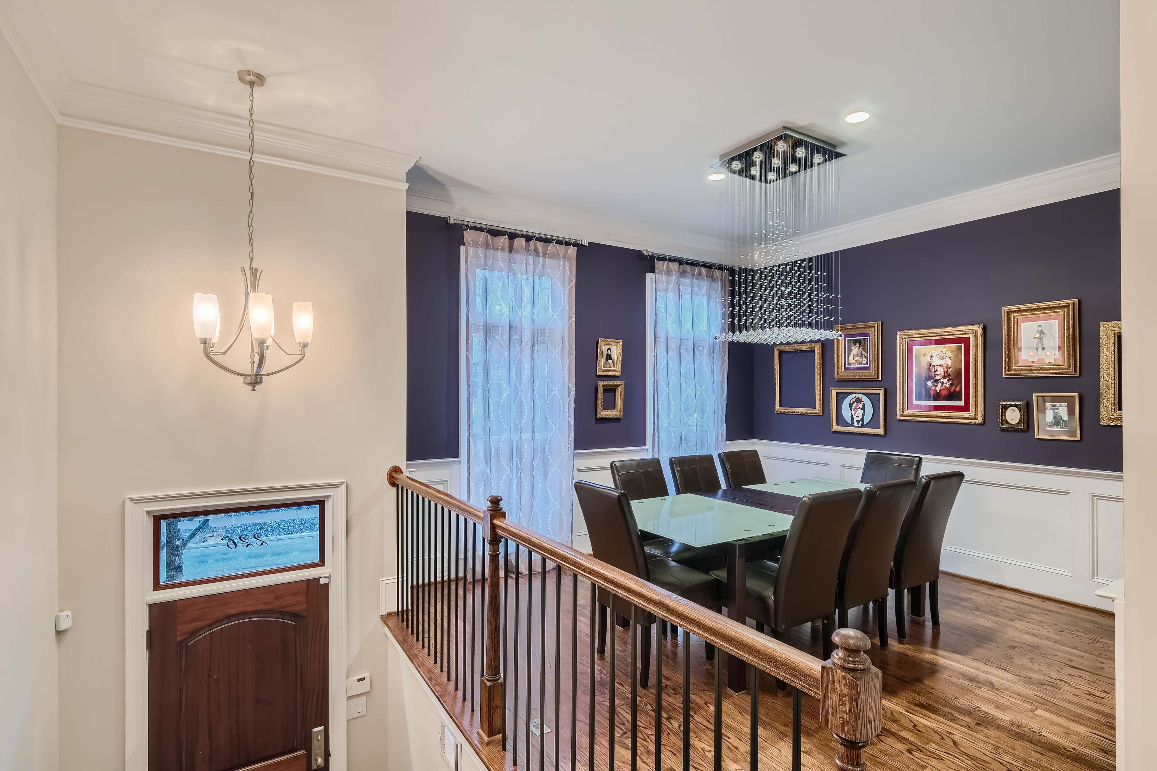 A modern dining area features a glass table surrounded by dark chairs, with framed artwork on the walls and a chandelier above.