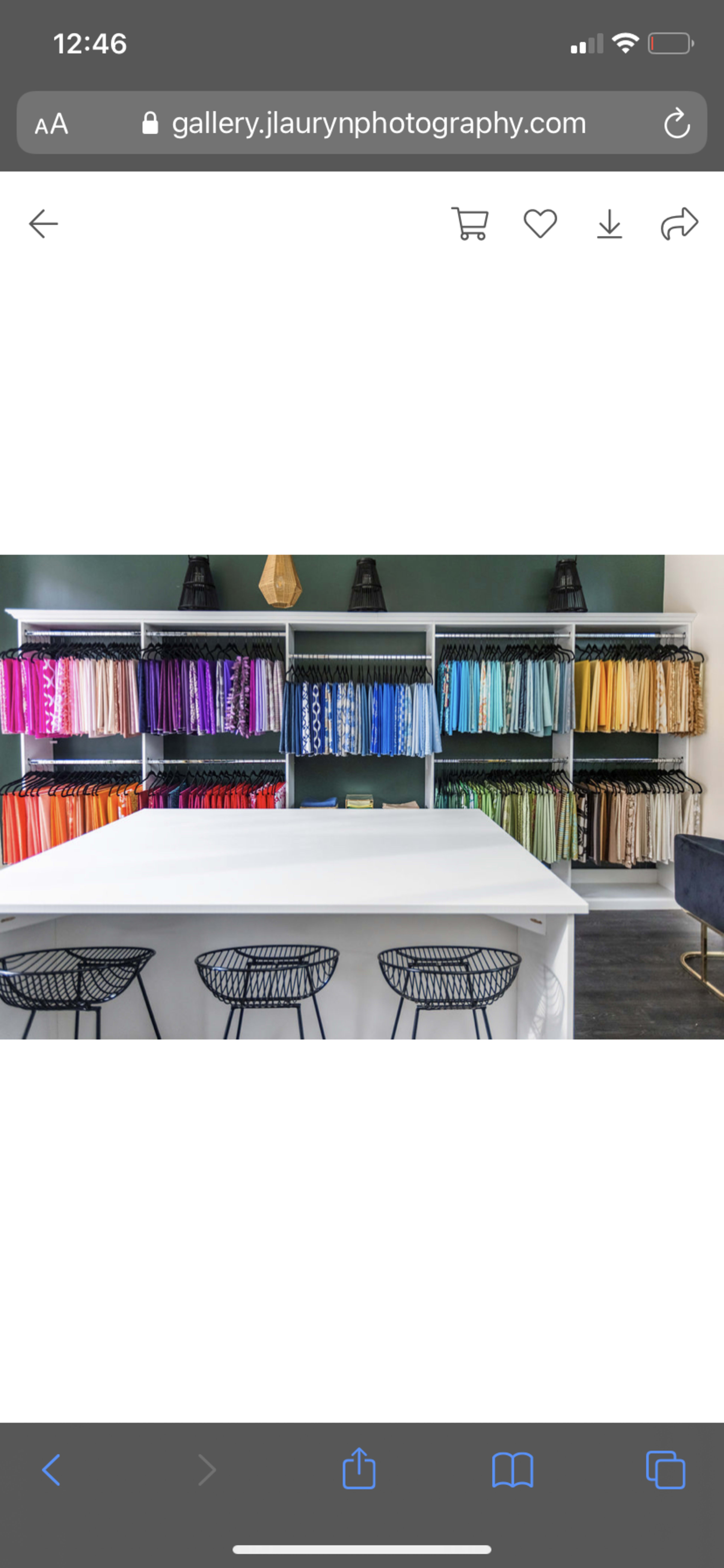 A retail space features neatly organized shelves displaying a gradient of colorful clothing arranged by hue.