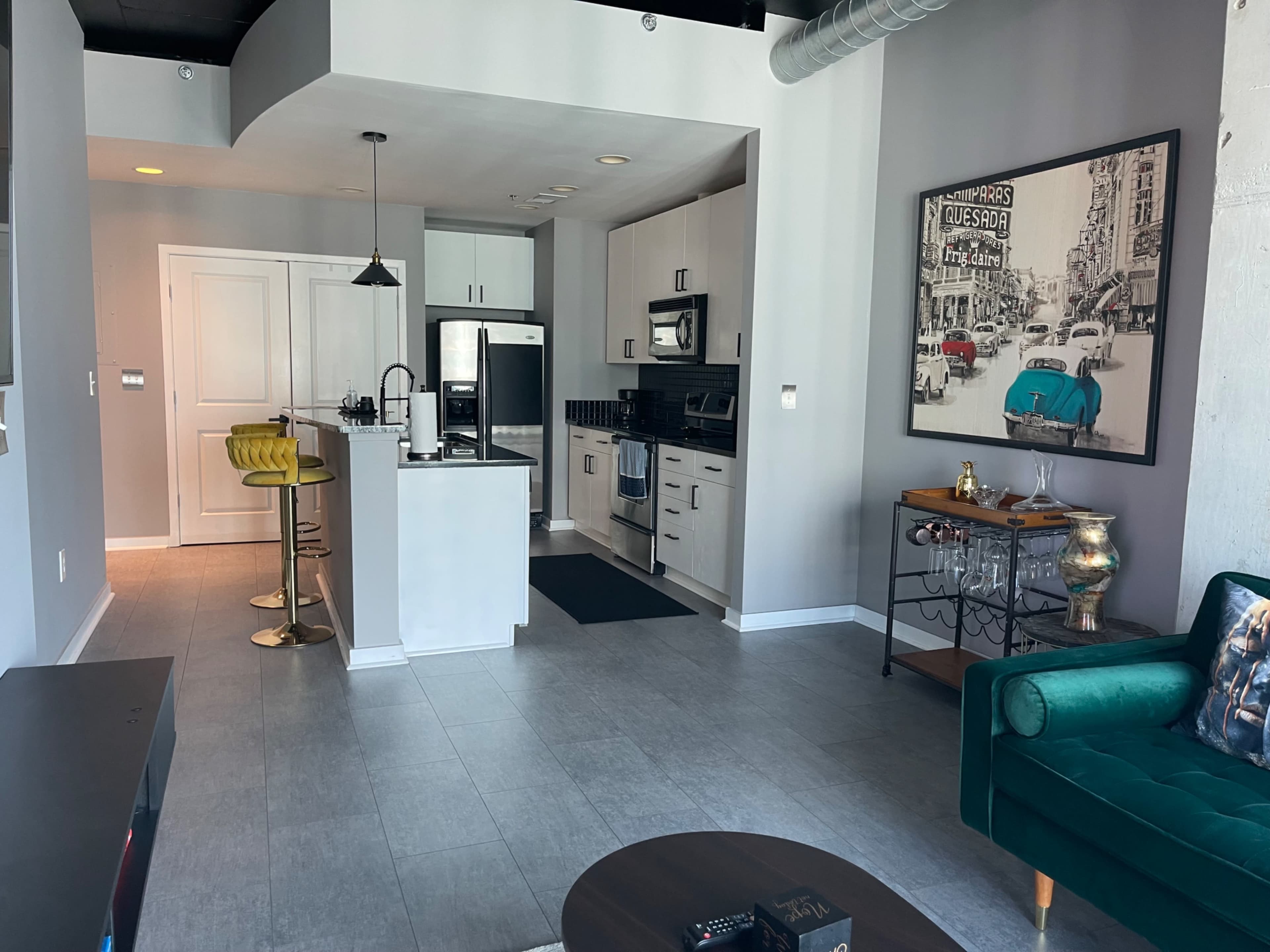 The image shows a modern, open-concept kitchen and living area with a small dining space and contemporary furnishings.