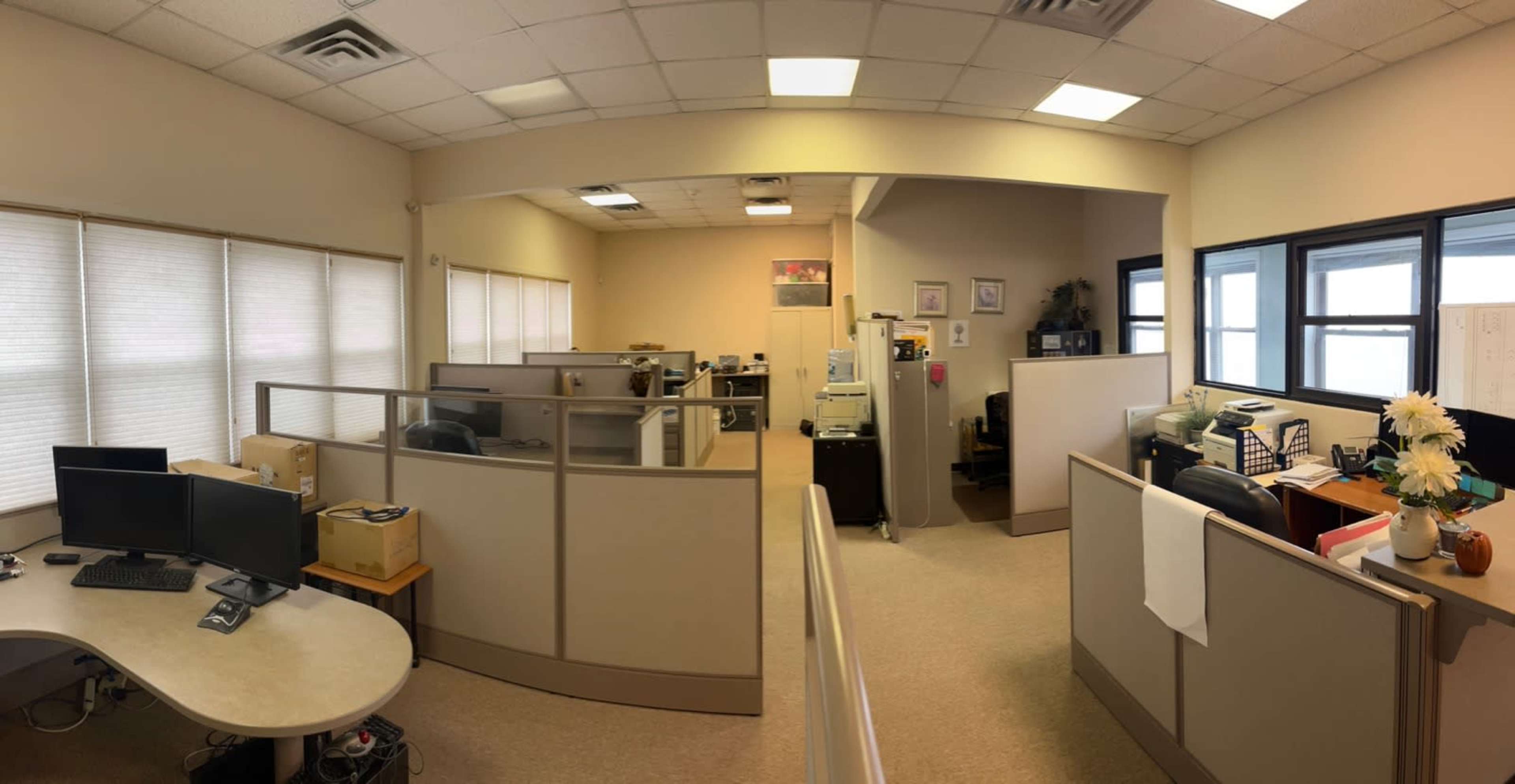 A panoramic view of a cubicle office space with several workstations, computers, and office equipment.