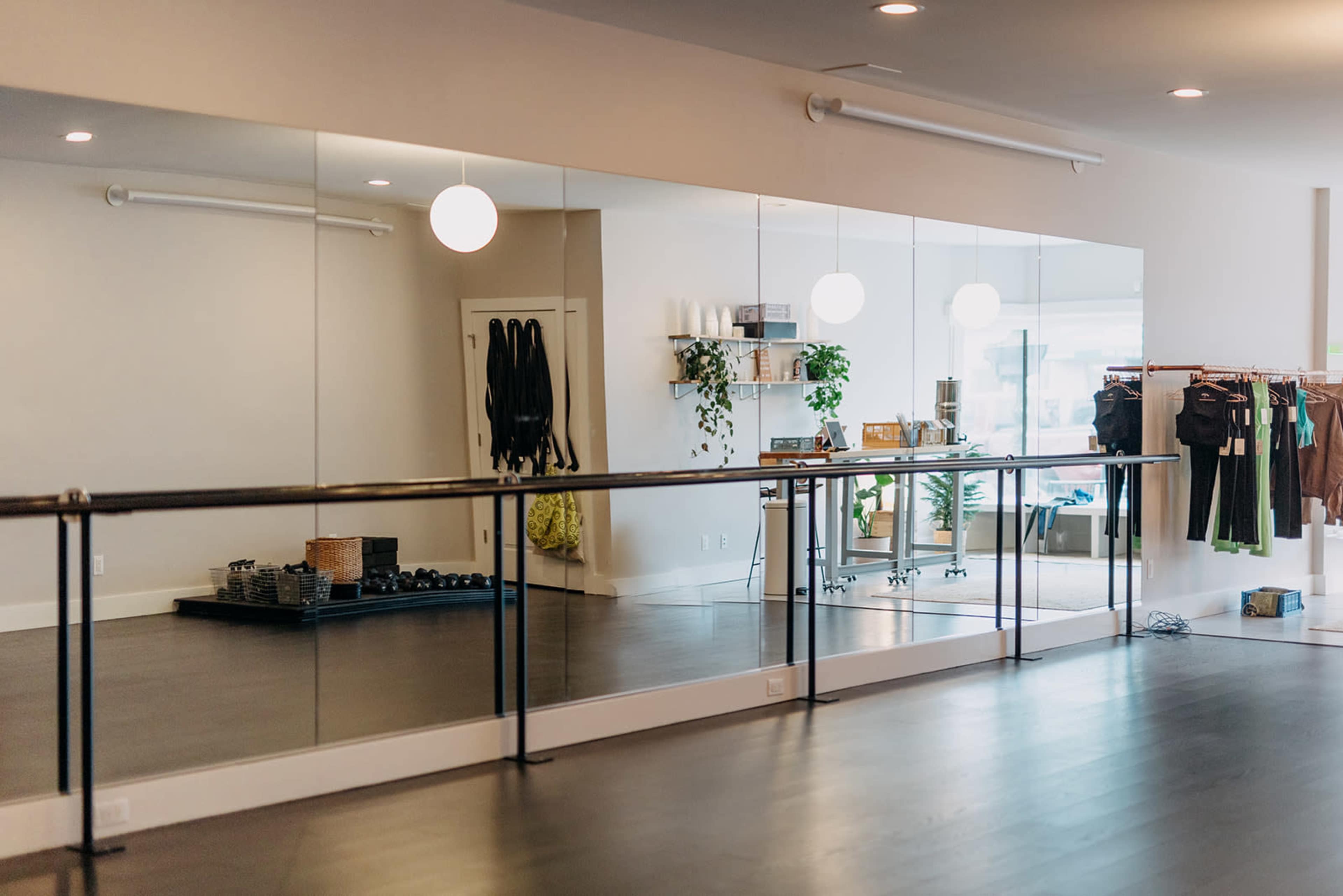 A fitness studio is equipped with large mirrors, exercise mats, dumbbells, and clothing racks along the wall.