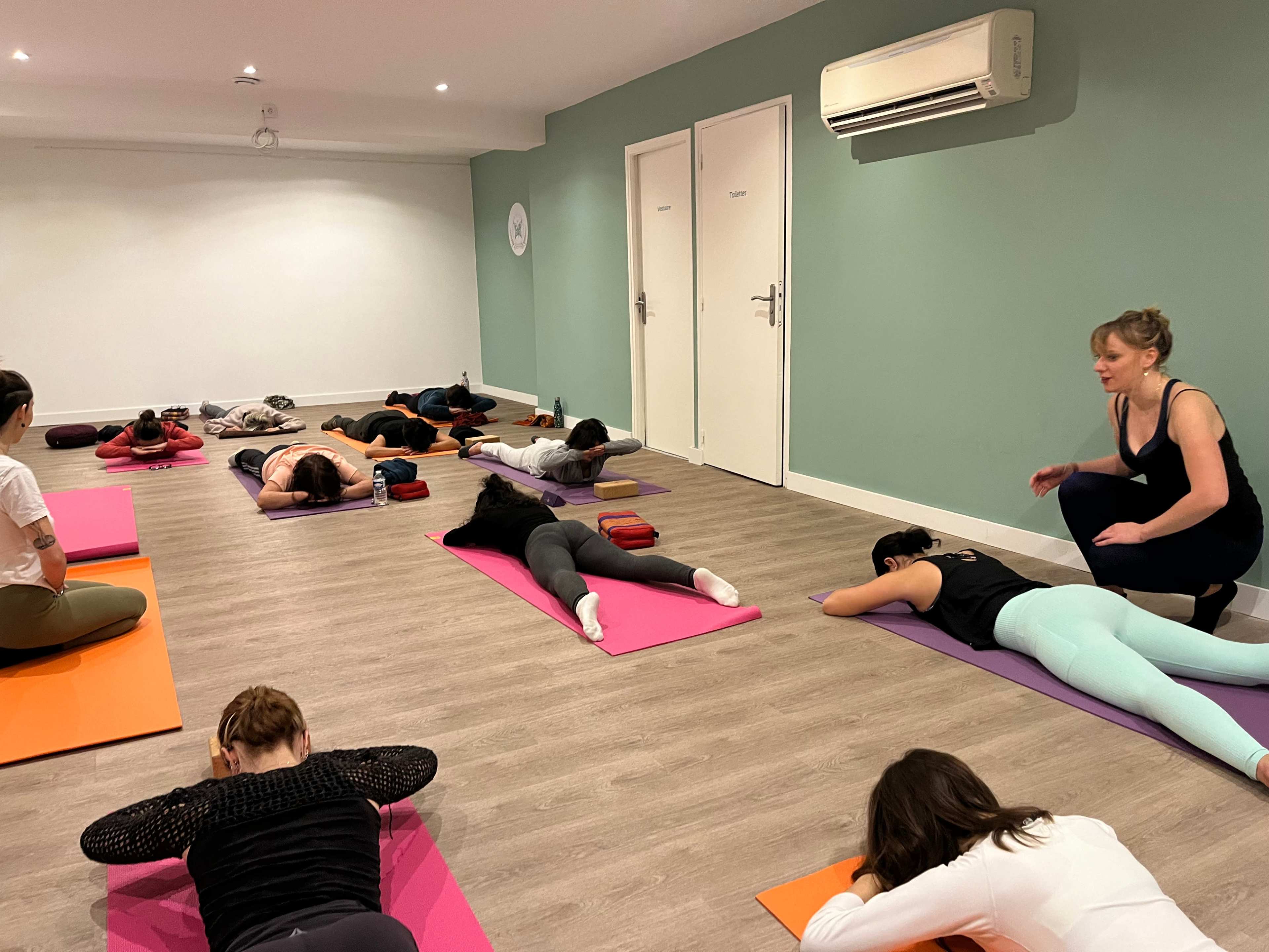 A group of people is participating in a yoga class on colorful mats in a brightly lit room.
