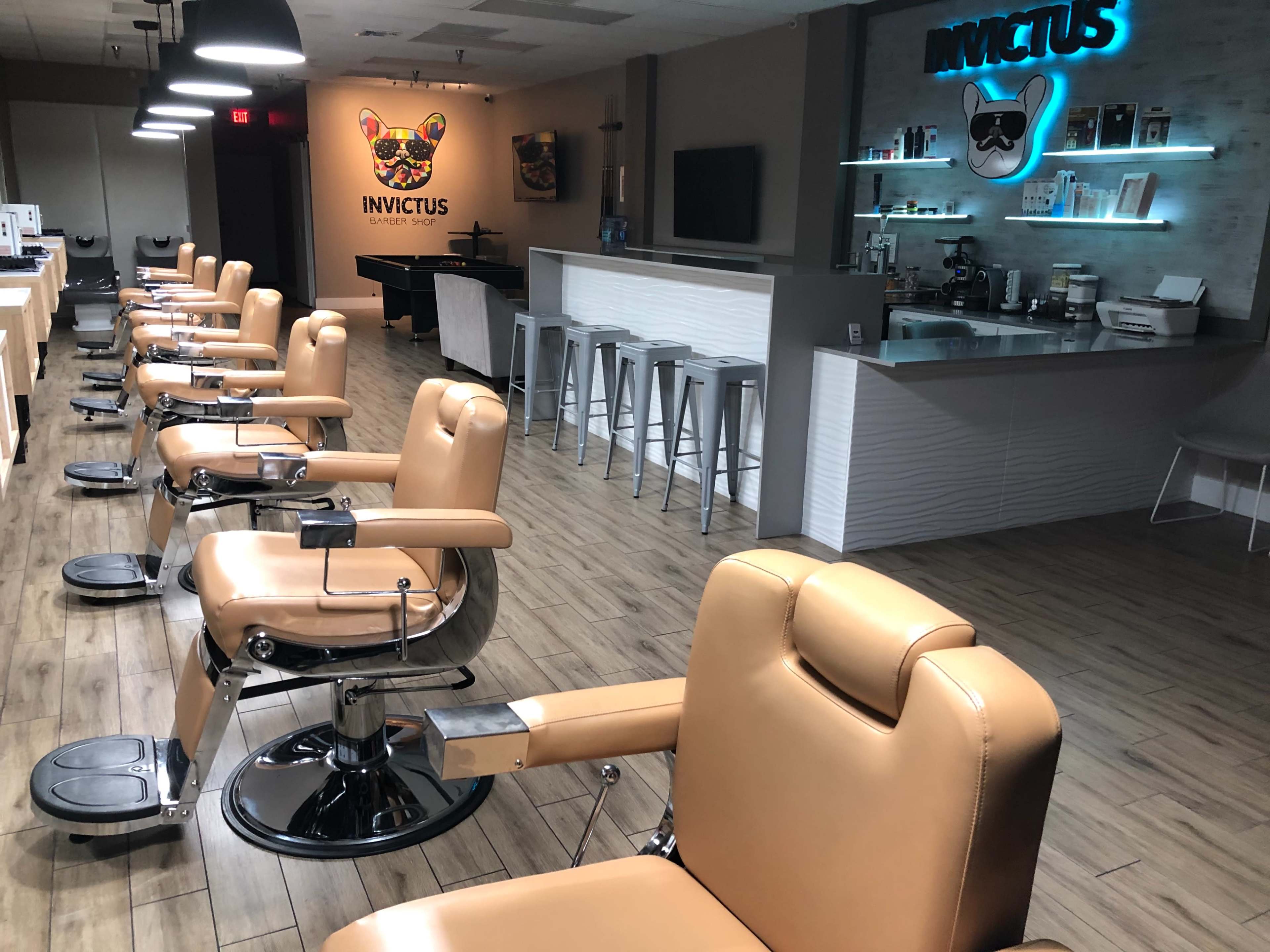 A barbershop interior with eight leather barber chairs arranged in a row, a sleek counter with a coffee station, and wall art featuring a dog logo.