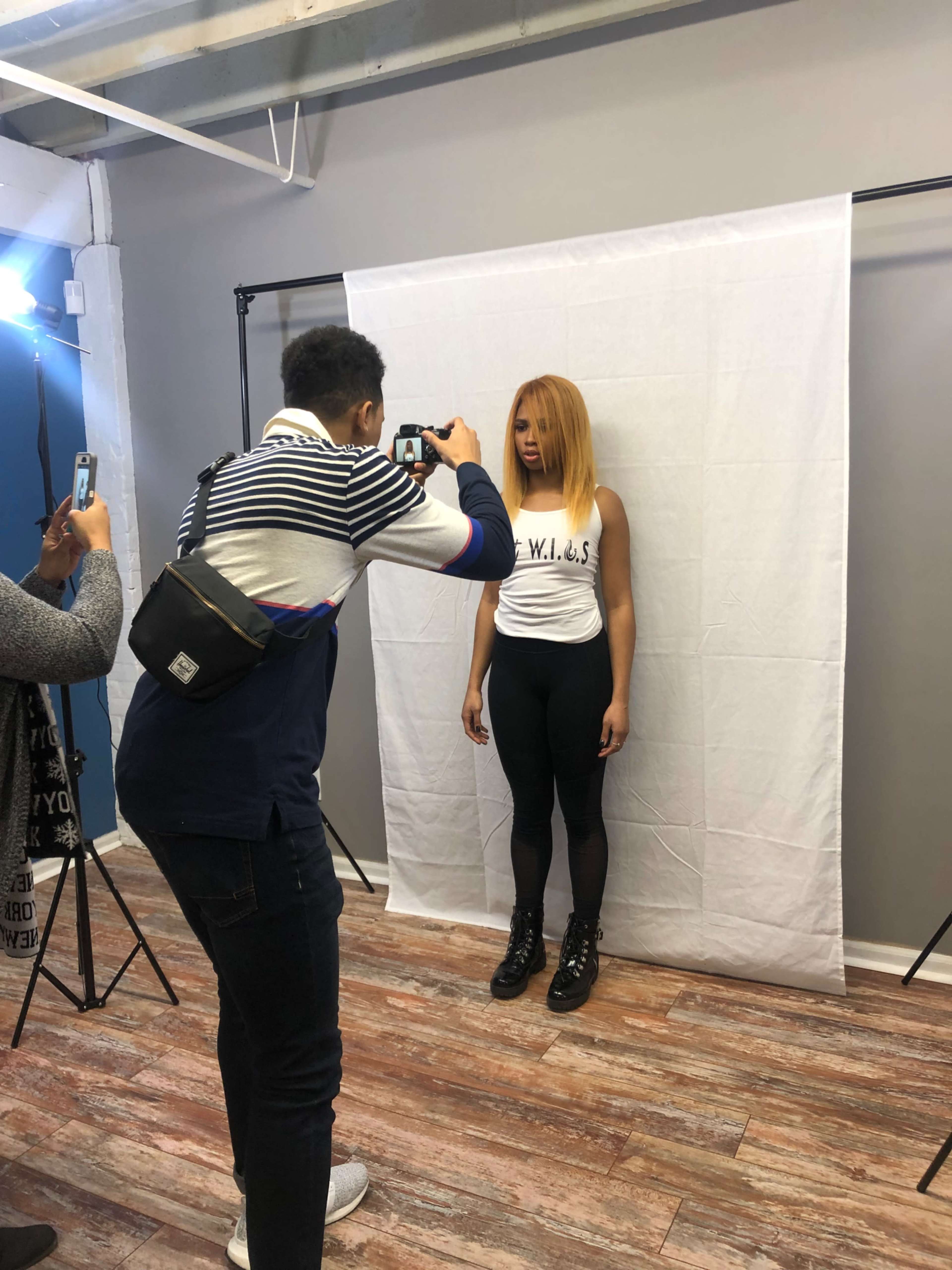 A photographer captures a model posing against a white backdrop in a studio.