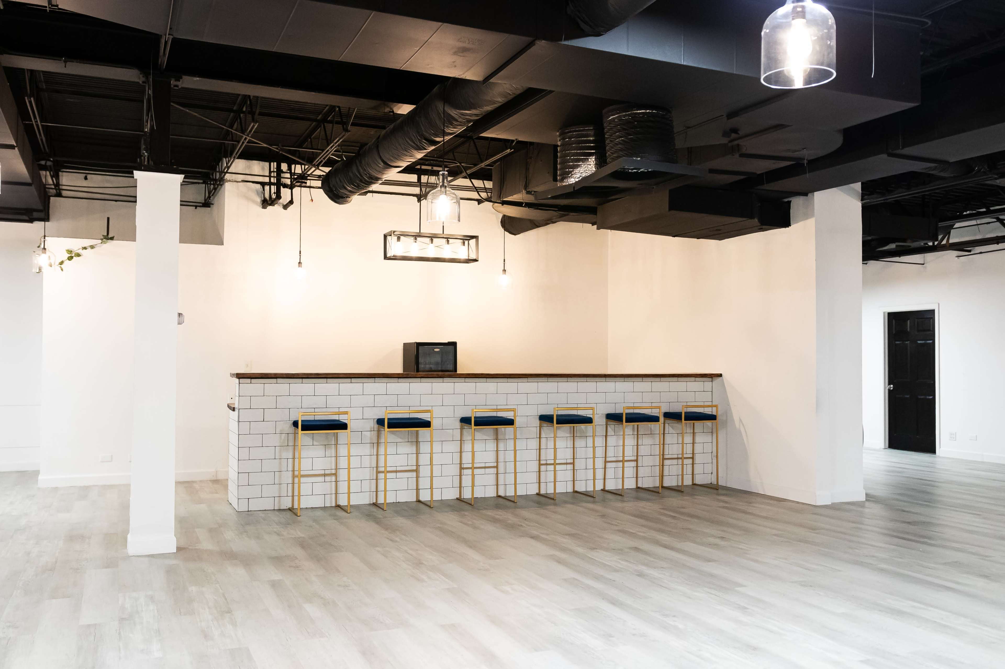 The image shows a minimalist, modern interior with a bar counter and high stools in an empty room featuring white walls and wooden flooring.