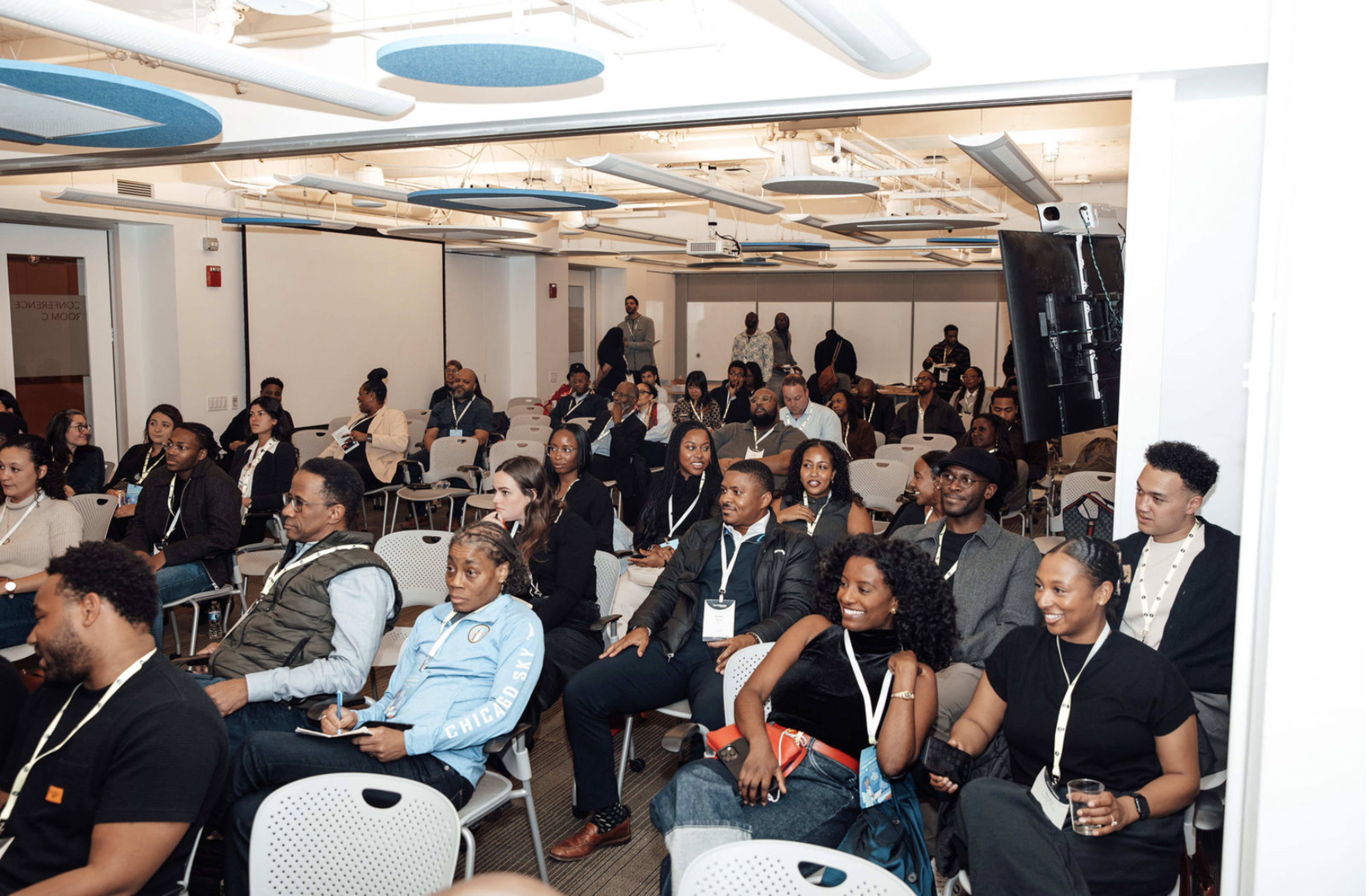 A group of people is seated in a conference room, engaging in a presentation or discussion.