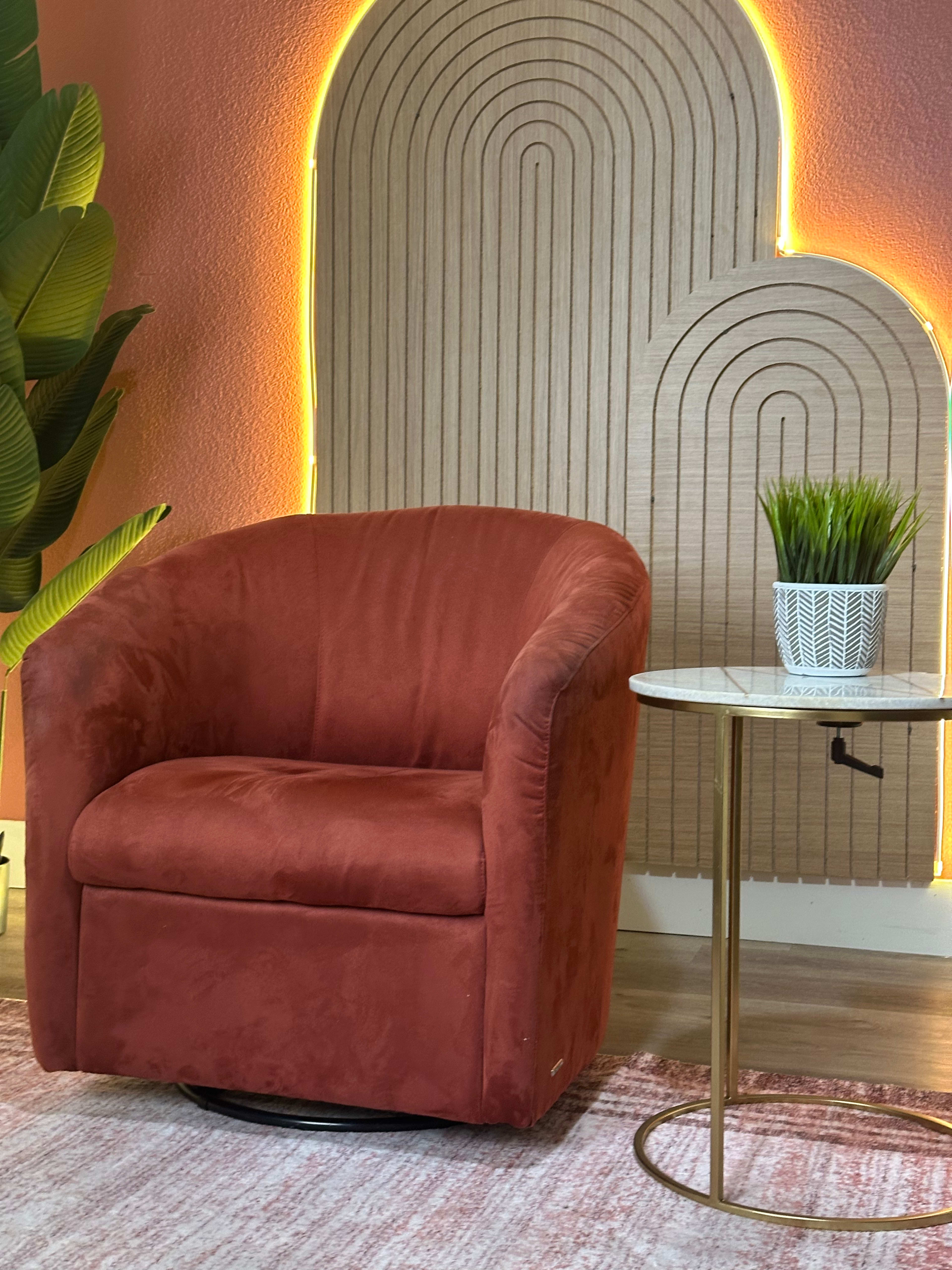 The image shows a cozy red swivel chair next to a small round table with a white pot containing a green plant against a textured wall with arched wood paneling illuminated by soft lighting.