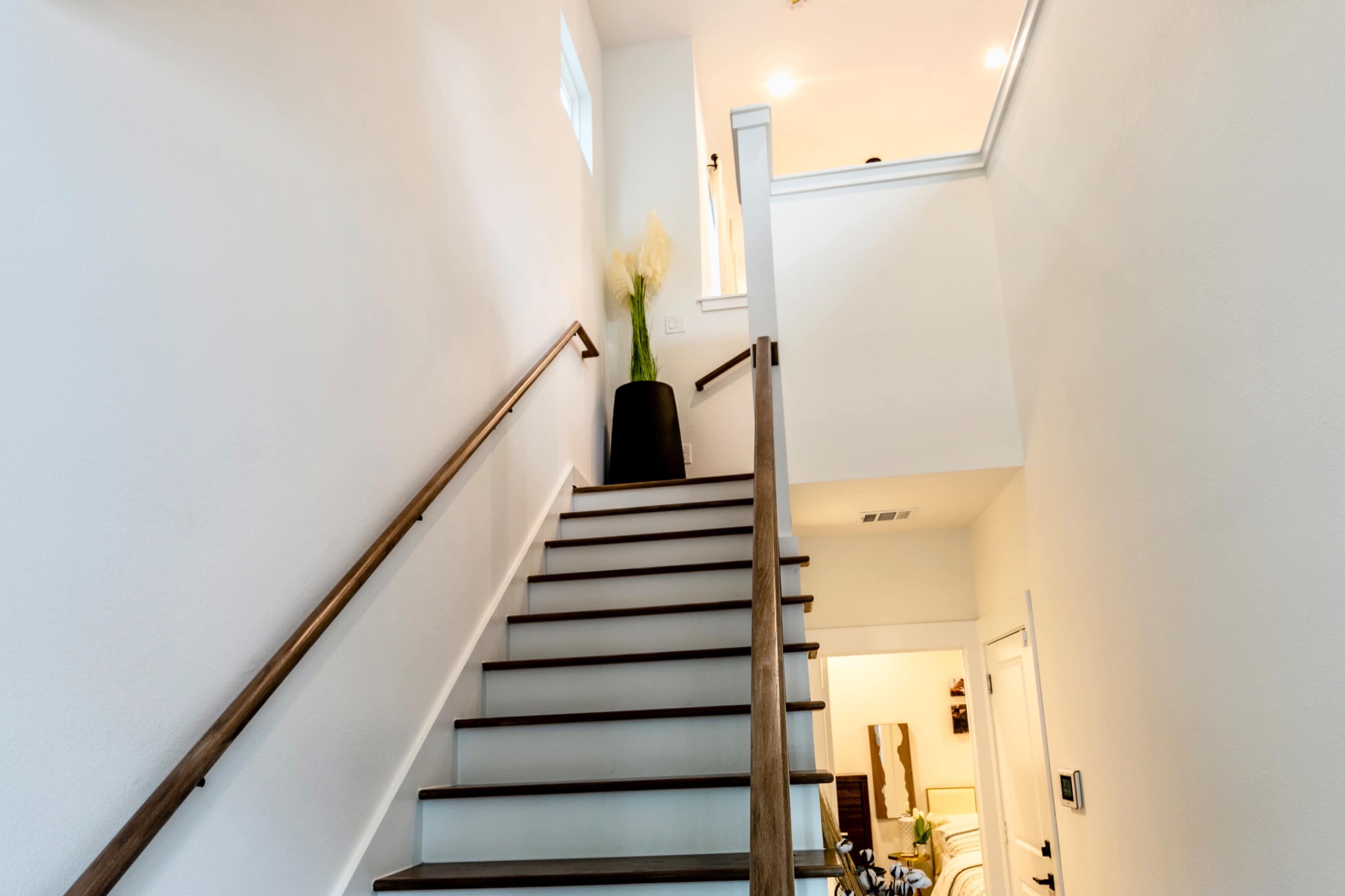 A set of wooden stairs leads upward to a brightly lit second floor, with a potted plant at the landing.