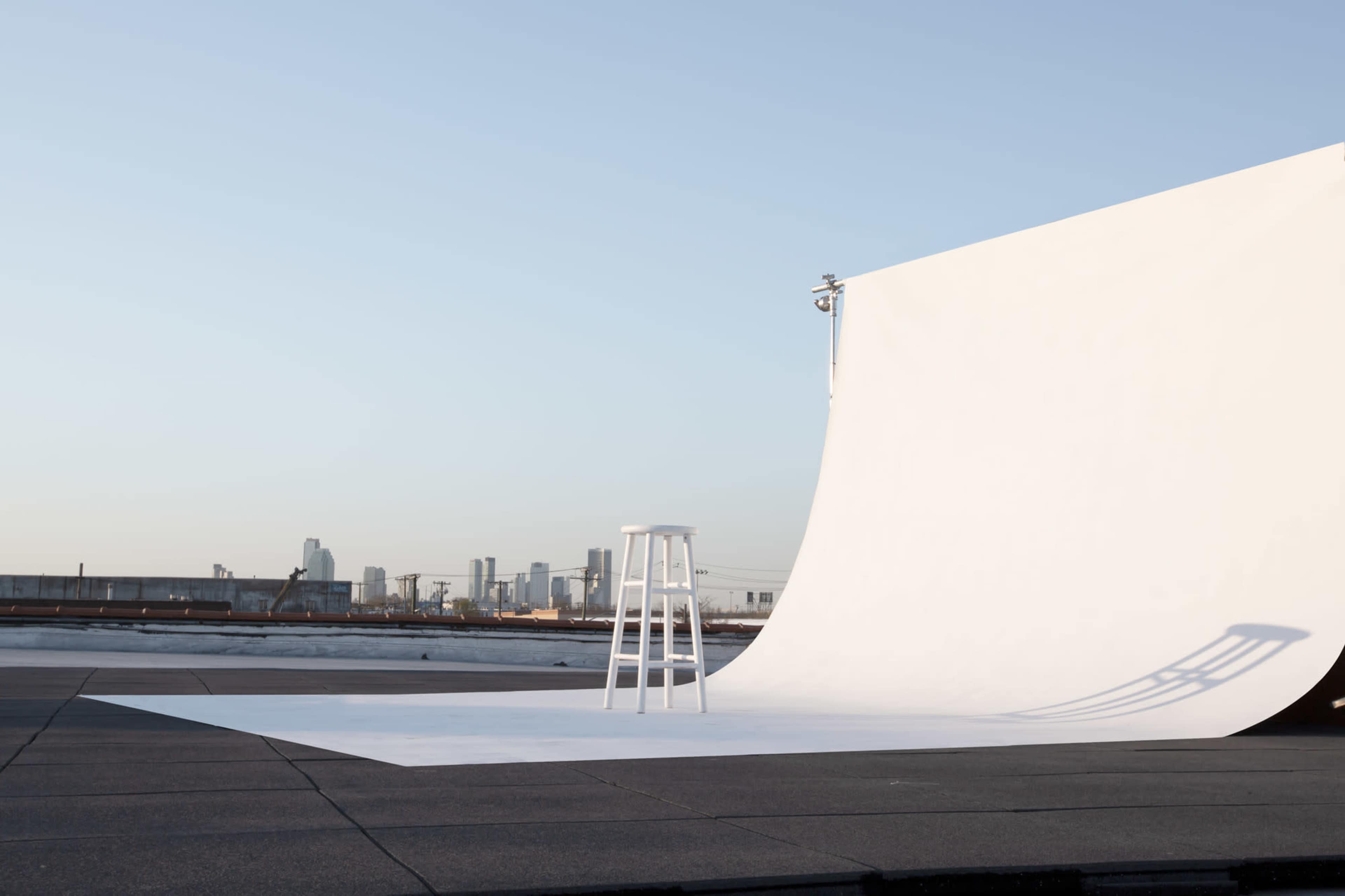 A white backdrop and stool are set up on a rooftop with a city skyline in the distance.