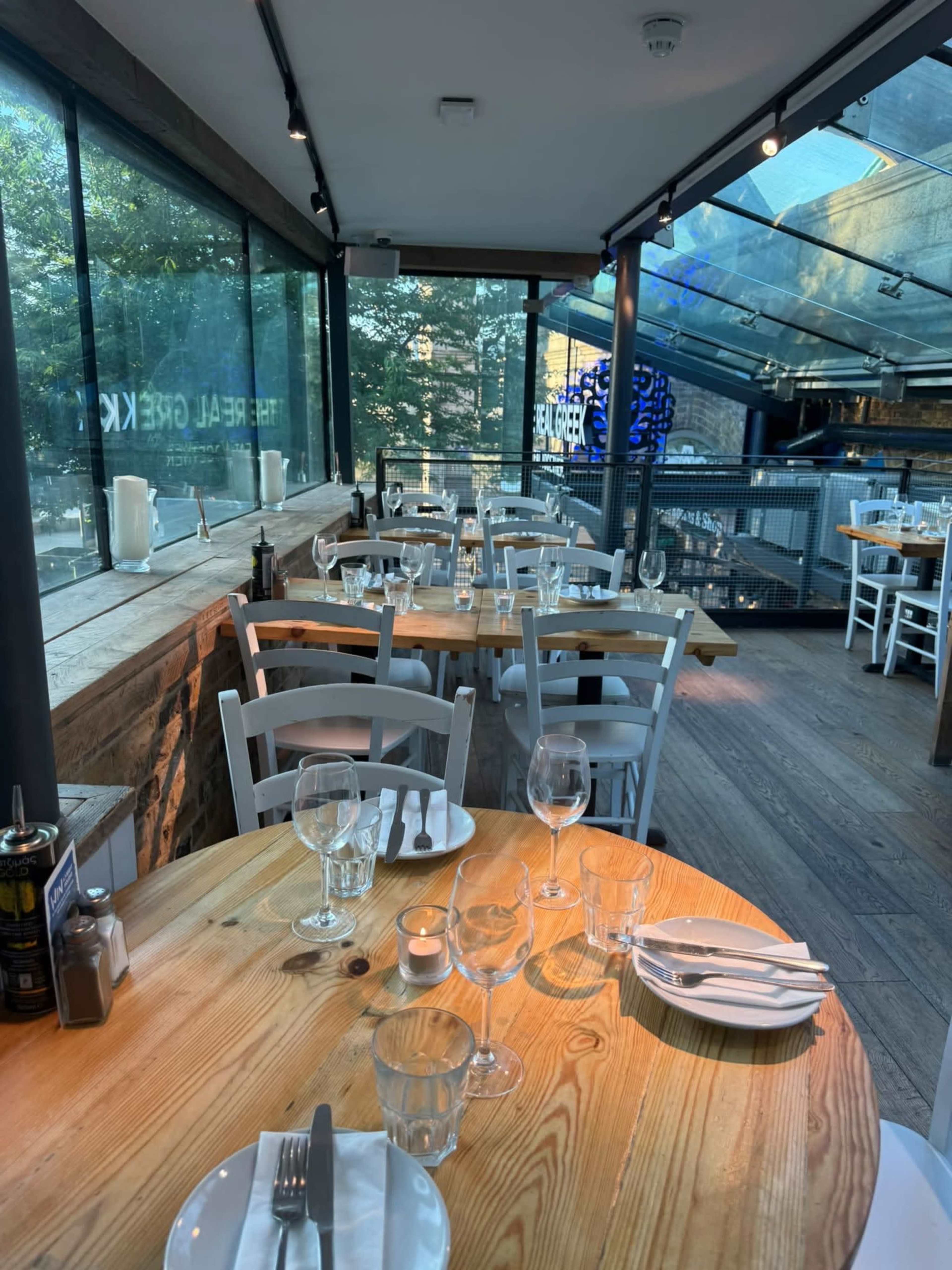 The image shows an indoor restaurant setting with wooden tables, white chairs, and large windows allowing natural light to fill the space.