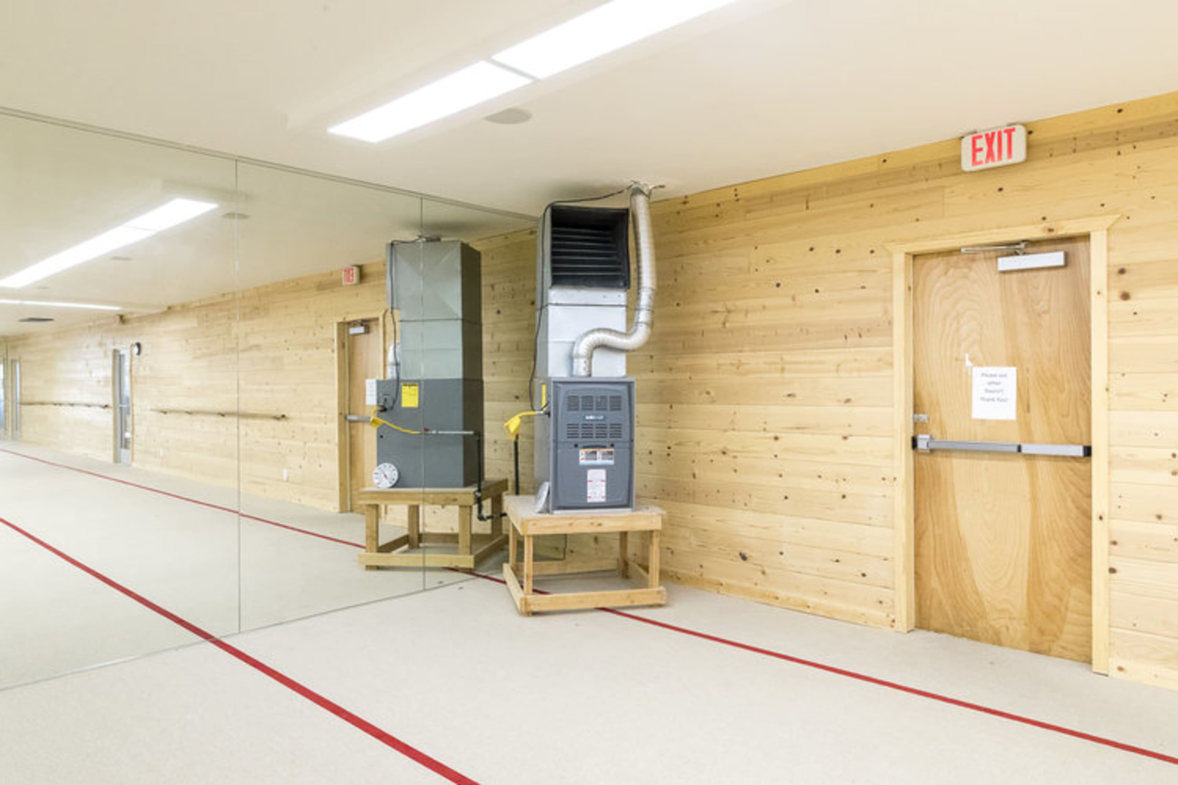 A hallway with wooden walls, a ventilation system on the left, and an exit door on the right.