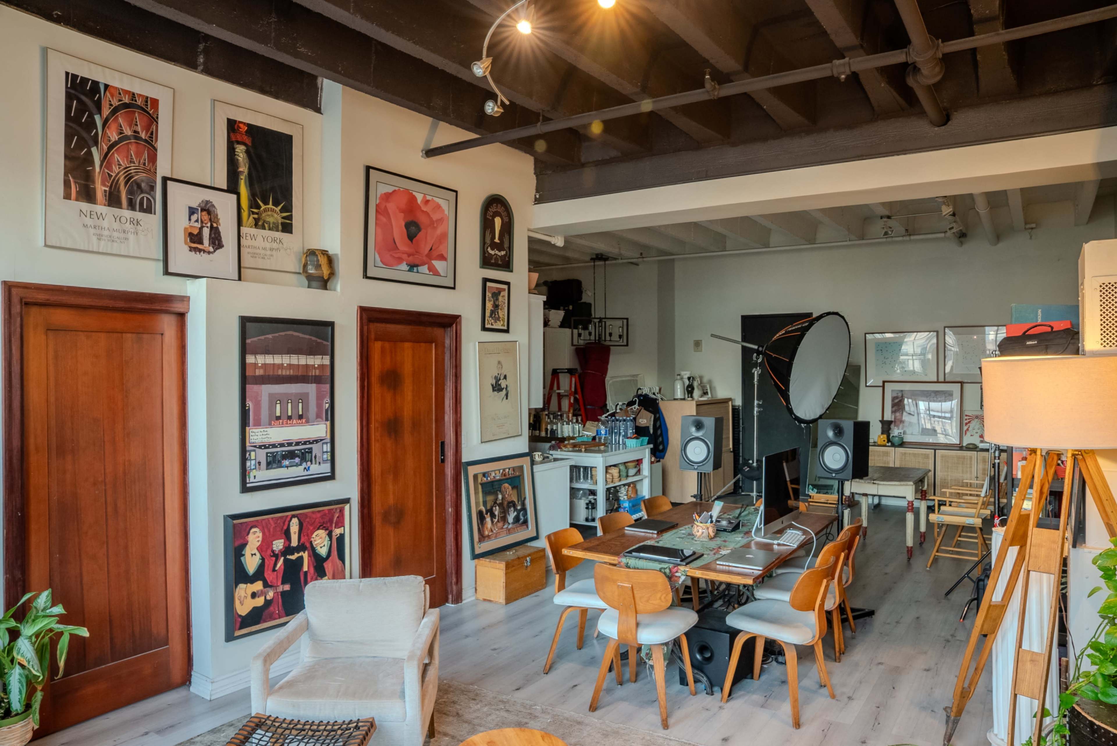 The image depicts a spacious room with wooden doors, a large dining table surrounded by chairs, and various framed artworks adorning the walls.