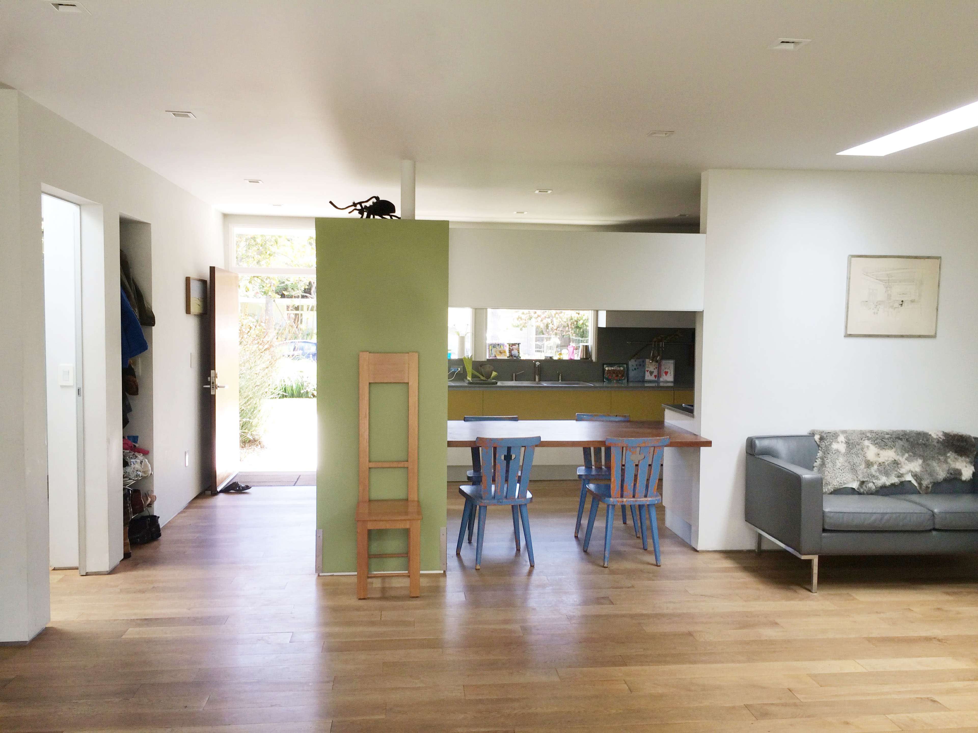 An open-plan living space with a seating area, a kitchen, and a dining area featuring a wooden floor and minimalistic furniture.